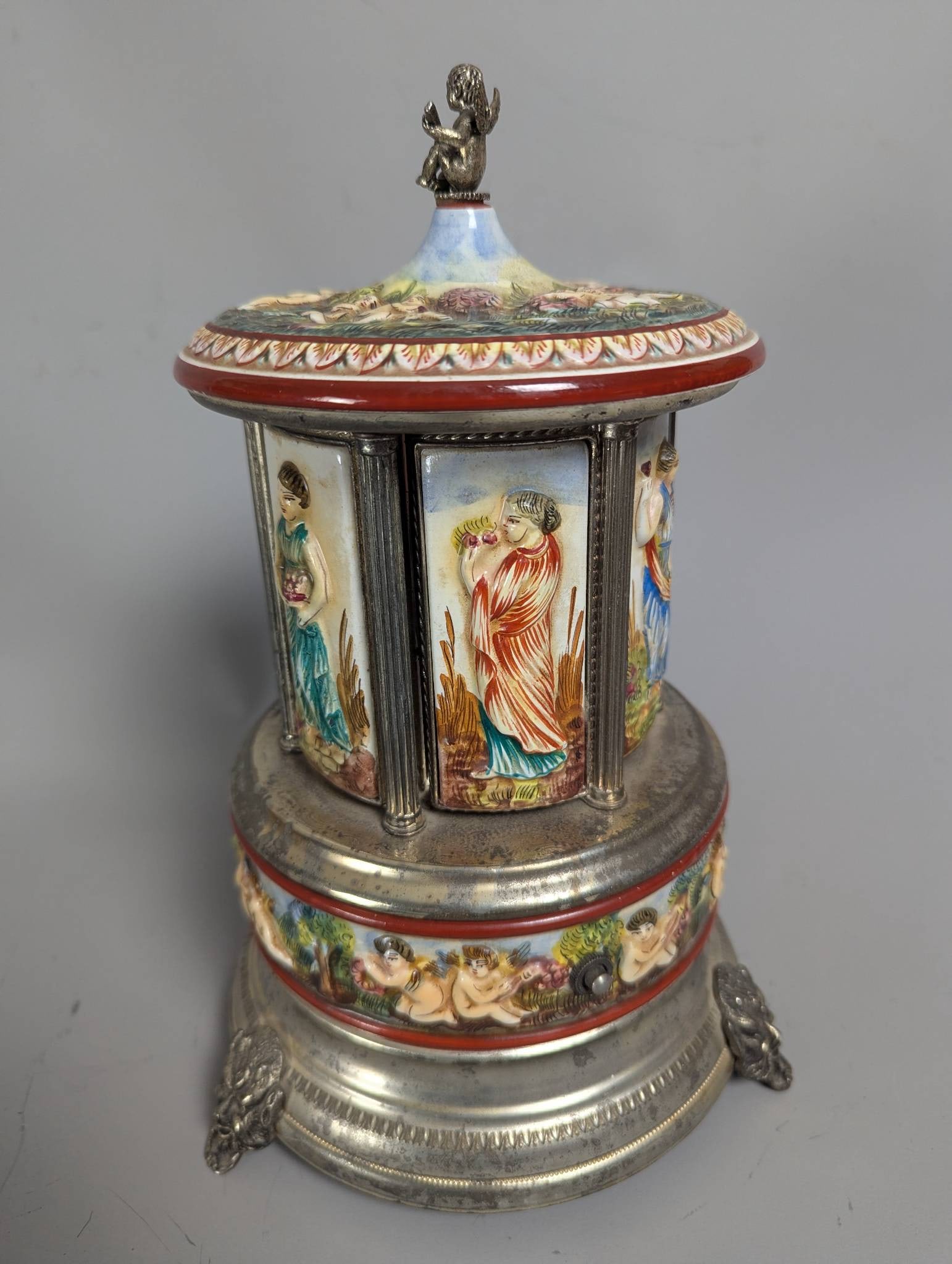 Reuge Capodimonte Porcelain Musical Cigarette or Lipstick Dispenser: Vintage Reuge Capodimonte musical cigarette or lipstick carousel dispenser, featuring a Swiss musical movement mechanism. Made in Italy, this porcelain piece is hand-painted with figural and cherub de