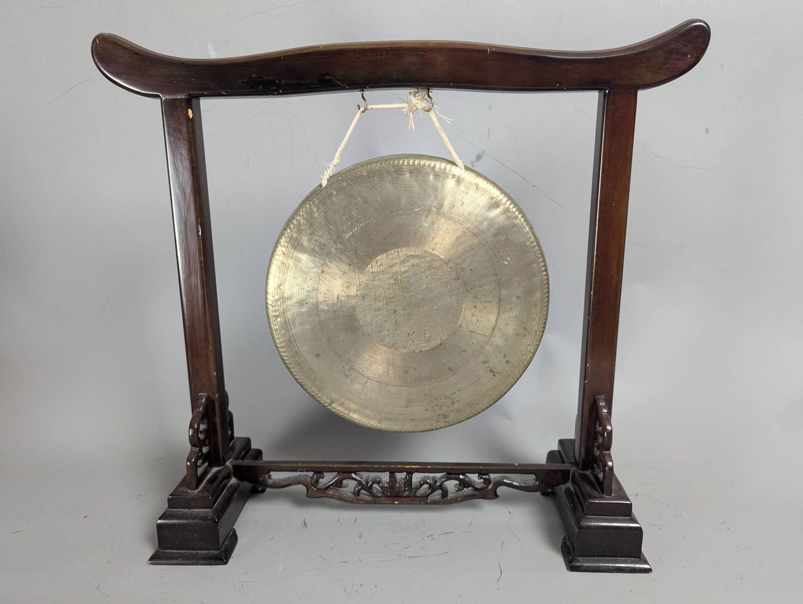 Antique Chinese Brass Gong on Carved Hardwood Stand: Antique Chinese brass gong presented on a carved rosewood or hardwood stand. The stand showcases intricate openwork fretwork decoration at the base and detailed carving, potentially of dragons, on the