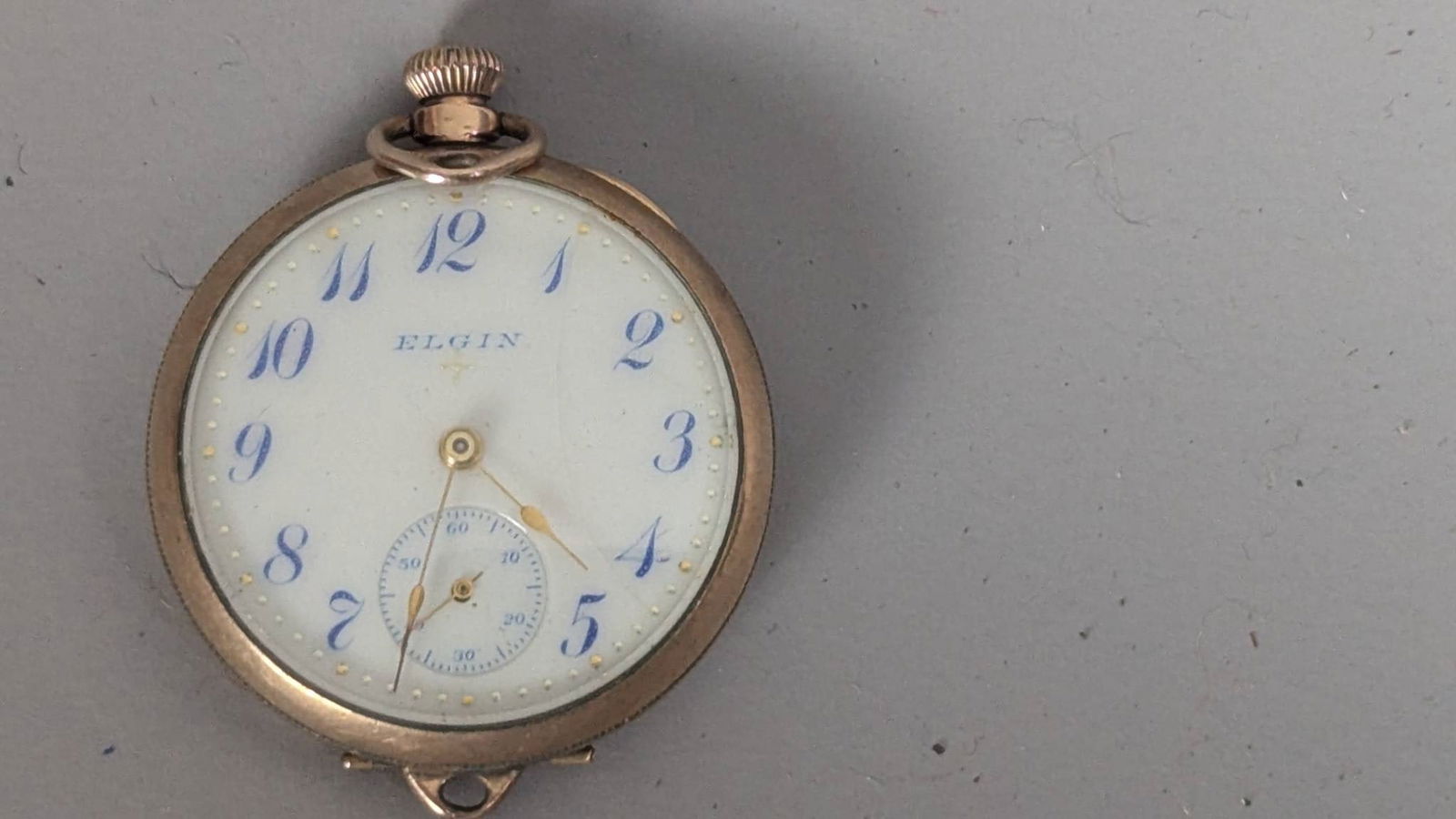Elgin Gold Filled Pocket Watch with Blue Numerals and Open-Face Design: Elgin pocket watch featuring a white enamel dial with blue numerals and gold-tone hands. It includes a 15-jewel movement marked Elgin, USA, and the case is stamped inside with a Hufco hallmark and