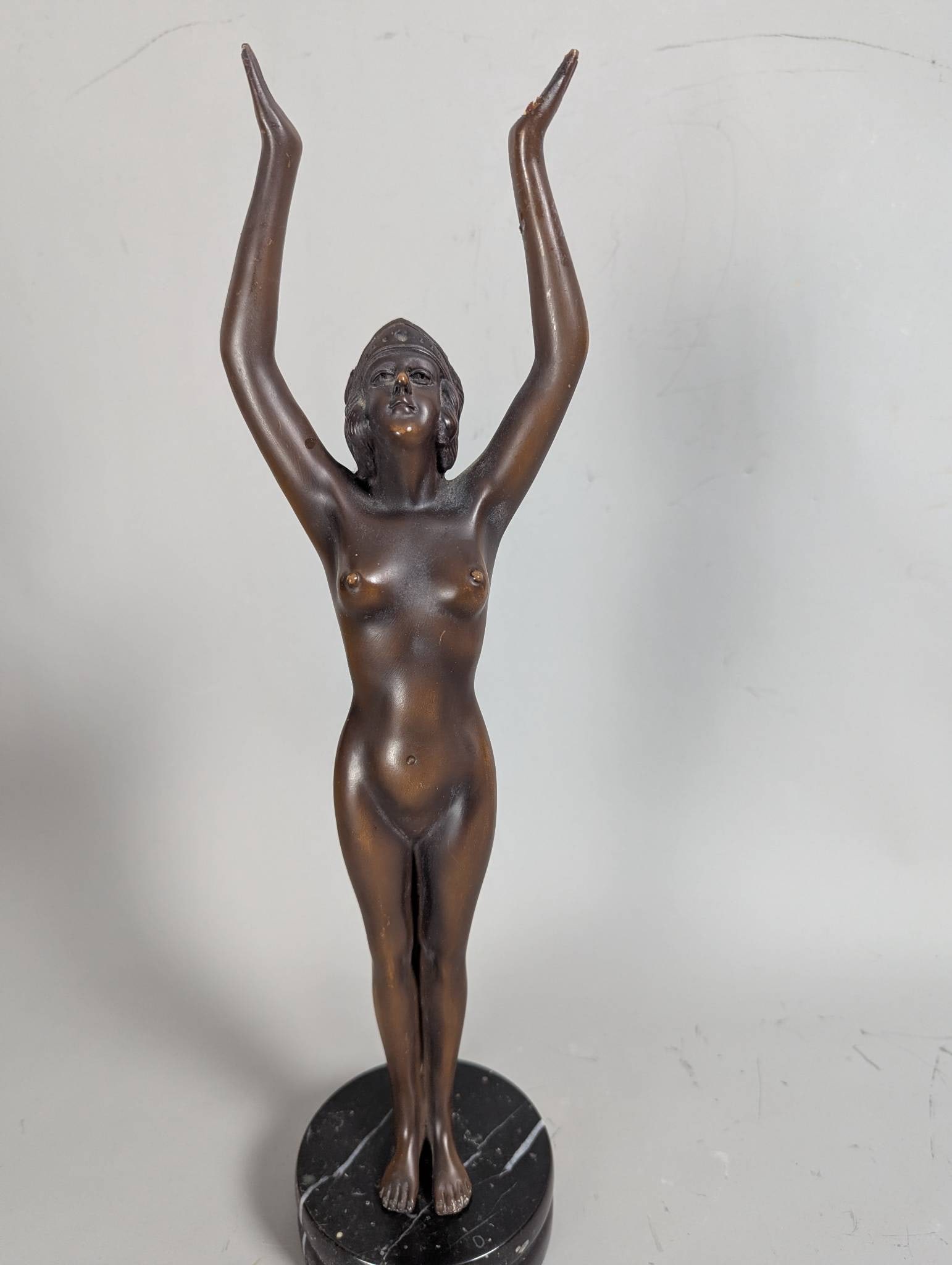 Bronze Sculpture of Nude Woman with Outstretched Arms on Black Marble Base: **Important** Please read below description on how to avoid high shipping costs. A bronze sculpture of a nude woman standing in a pose with her arms raised high above her head. The figure is crafted i