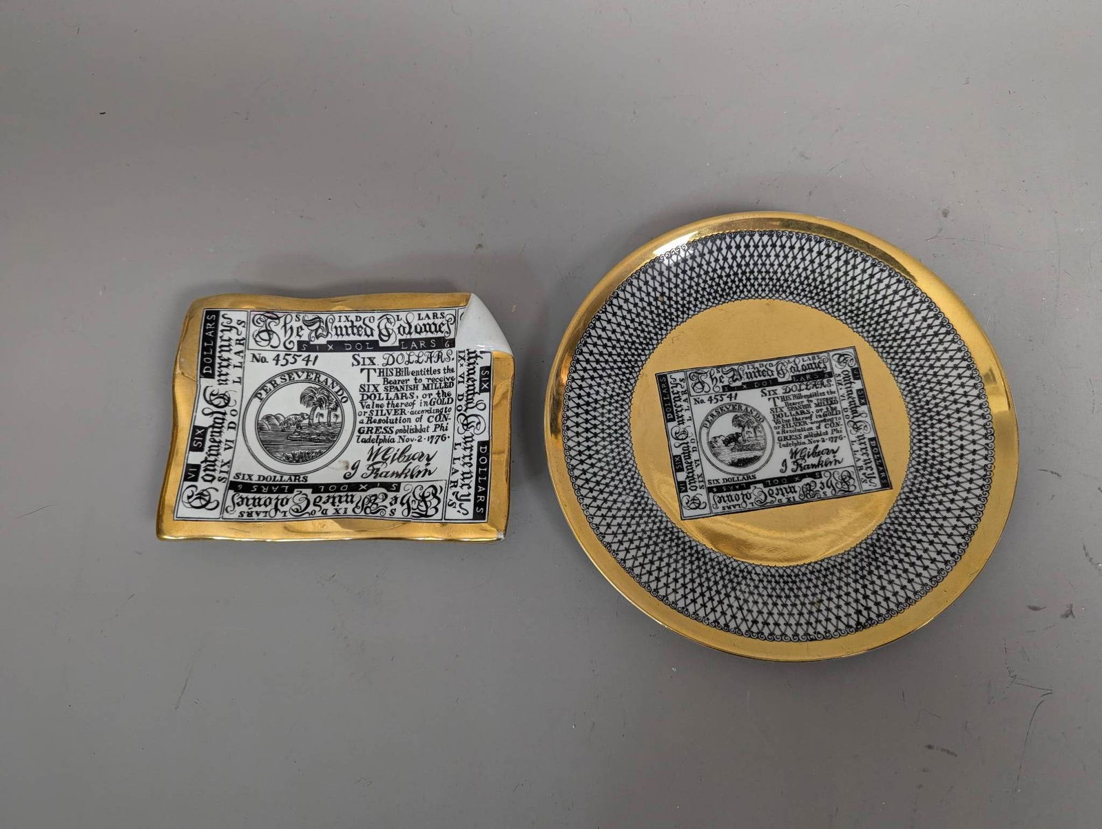 Piero Fornasetti Porcelain Plate & Ashtray with Continental Currency Design: Decorative porcelain set consisting of a plate and a dish or ashtray designed by renowned Italian artist Piero Fornasetti. The design features an intricate black and white trompe-l'oeil print of a 177