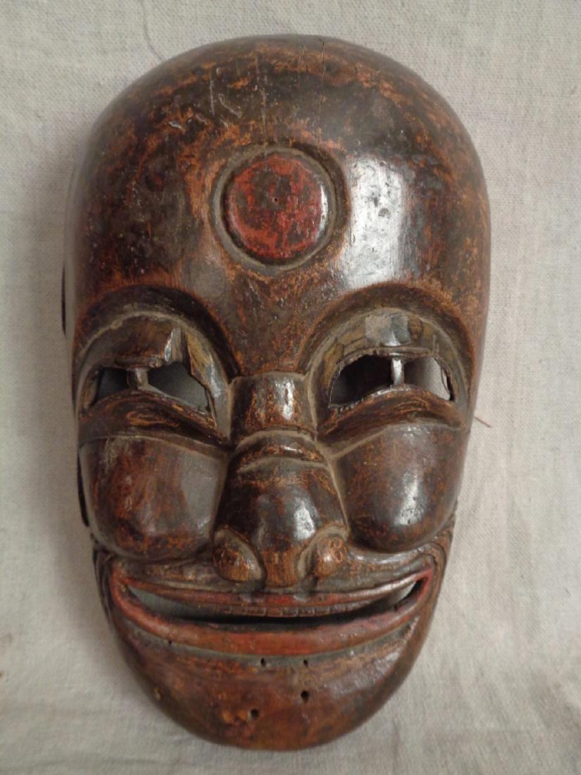 Antique Chinese Carved Wood Mask: Hand carved wood with old dark finish with details in red lacquer. Open carved eyes, nose, and mouth. Drilled holes along top of head and chin for missing fiber additions. Old loss of right ear. 9" L