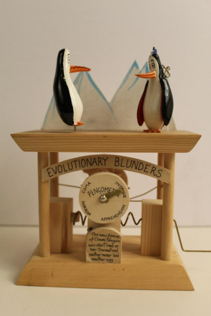 Neil Hardy Automata Sculpture Penguins: "Evolutionary Blunders", 2000. Wood, paint, ink, coiled metal, fishing line, and string. Signed and dated '00 to base. Turning handle moves "Pengometer" dial and penguins. Excellent condition. 8" H x 