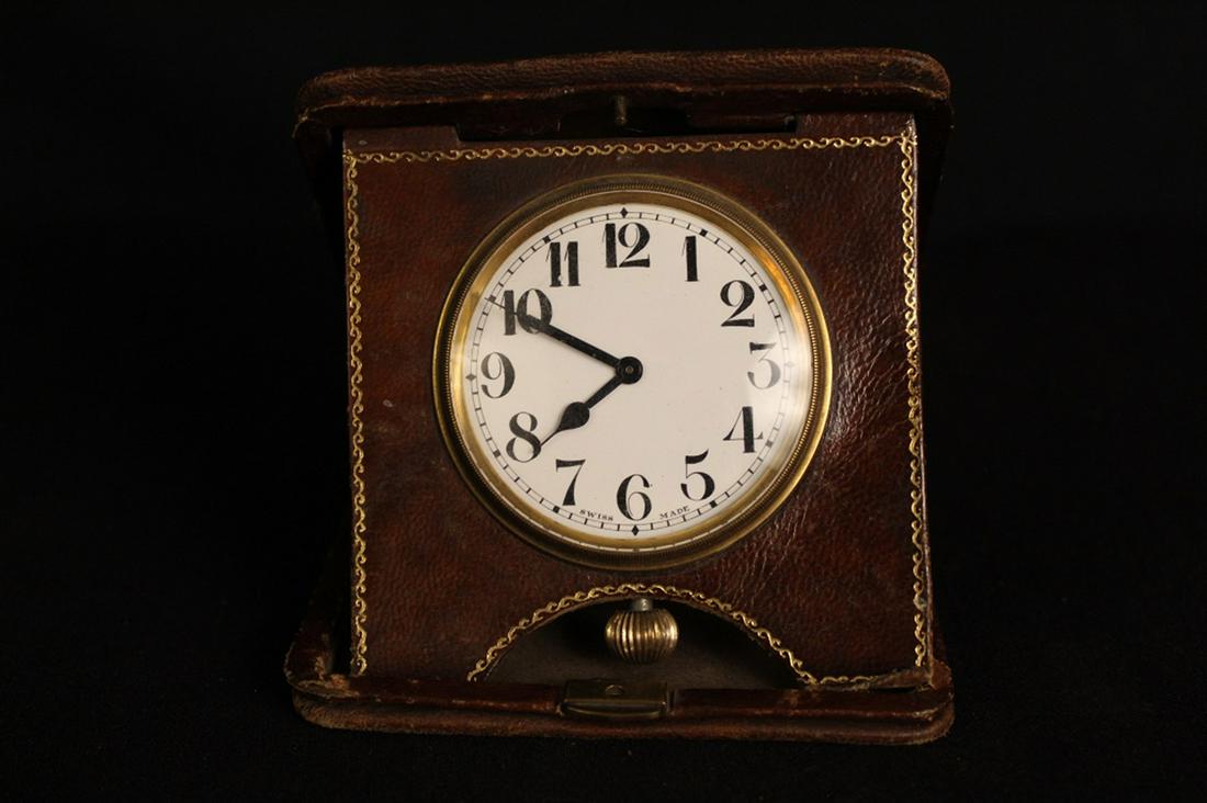 Antique Swiss Travel Folding Travel Clock: Clock marked "SWISS MADE" to porcelain face. Clock in excellent cosmetic condition; clock winds, hands are adjustable, but currently not running. Brown leather folding case in good condition (minor si