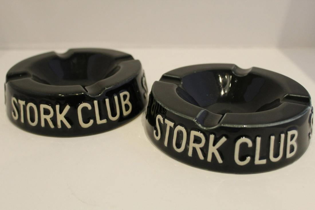 Two Vintage Stork Club Ceramic Ashtrays: Black gloss glaze with raised lettering in white. One stamped 56-12 to bottom. Signs of light use; no chips or cracks. 1.5" H x 5.25" dia. approx. each.
