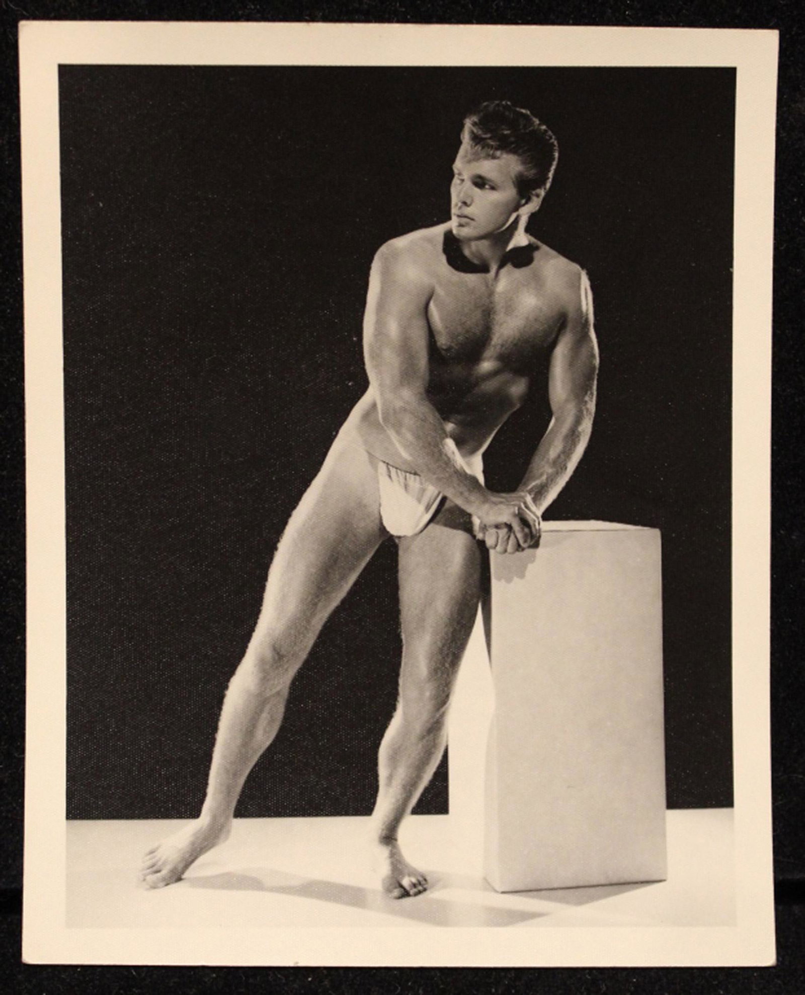 Bruce of Los Angeles Male Nude Physique Photo: Vintage 1950's photograph of George Tower in posing pouch leaning on pedestal. Stamped "Bruce 2129-5" with pen written name to reverse. Good sharp image on satin heavy weight paper. Excellent conditio