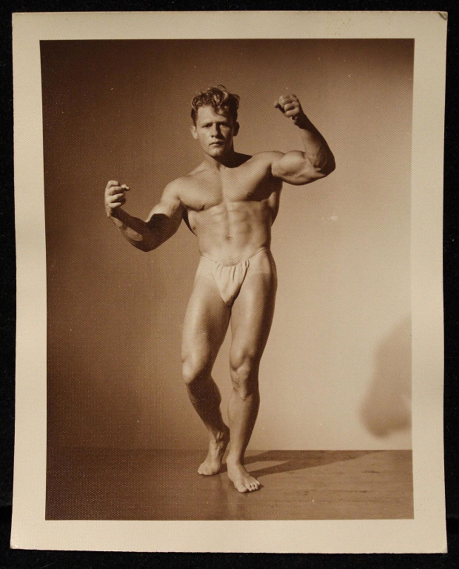 Early Bob Mizer AMG Male Nude Gene Meyer: Vintage late 1940's/ early 1950's photograph of Gene Meyer in posing pouch flexing. Stamped "T 11" to reverse. Good sharp image in sepia tone on satin heavy weight paper. Excellent condition. 5" x 4"