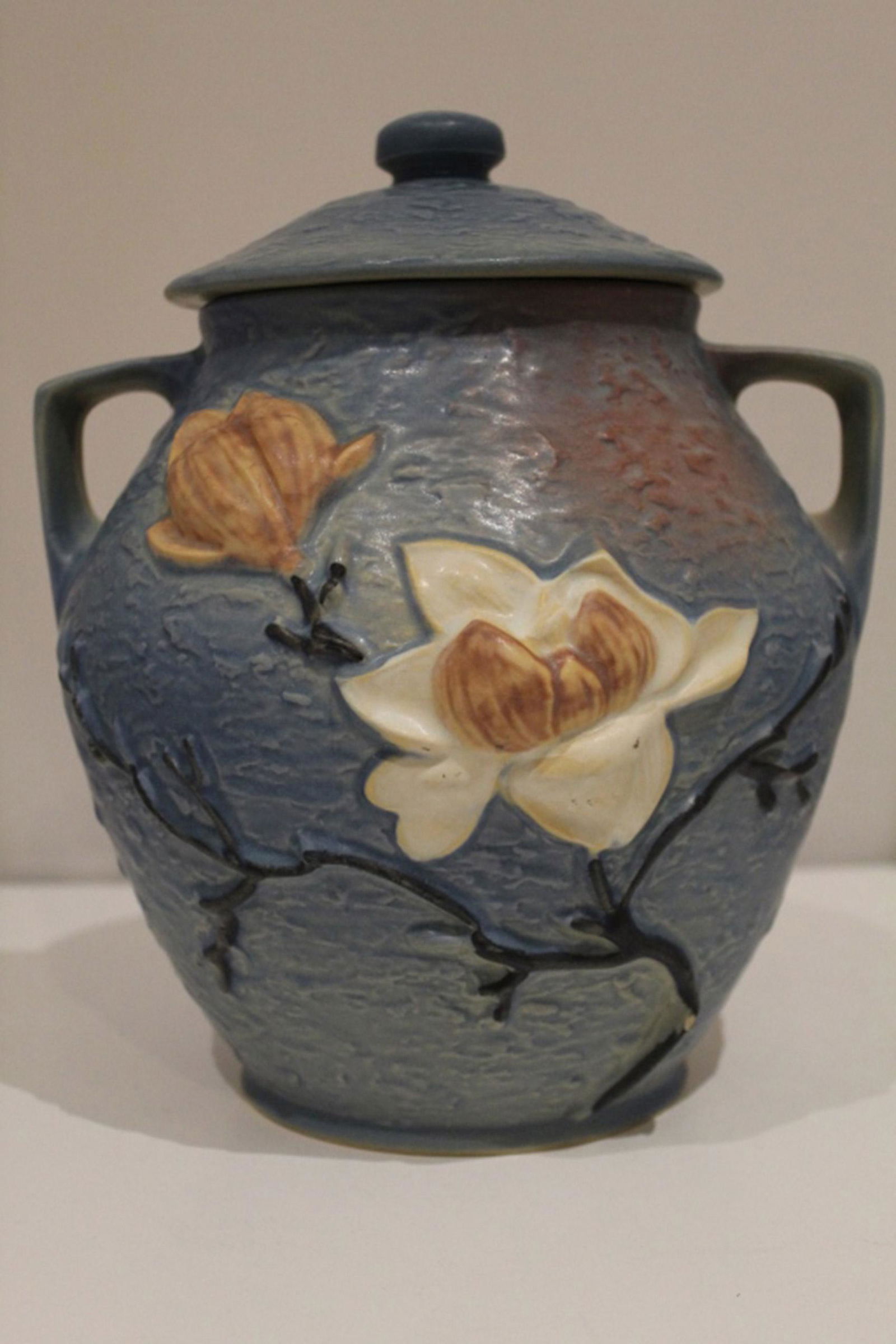 Roseville Pottery Magnolia Cookie Jar / Vase 2-8": Blue glaze lidded jar / vase. Raised Roseville marks to bottom. Glaze flaw or possible glaze flake to lid; base with small flake chip to stem on one side. Normal glaze crazing.