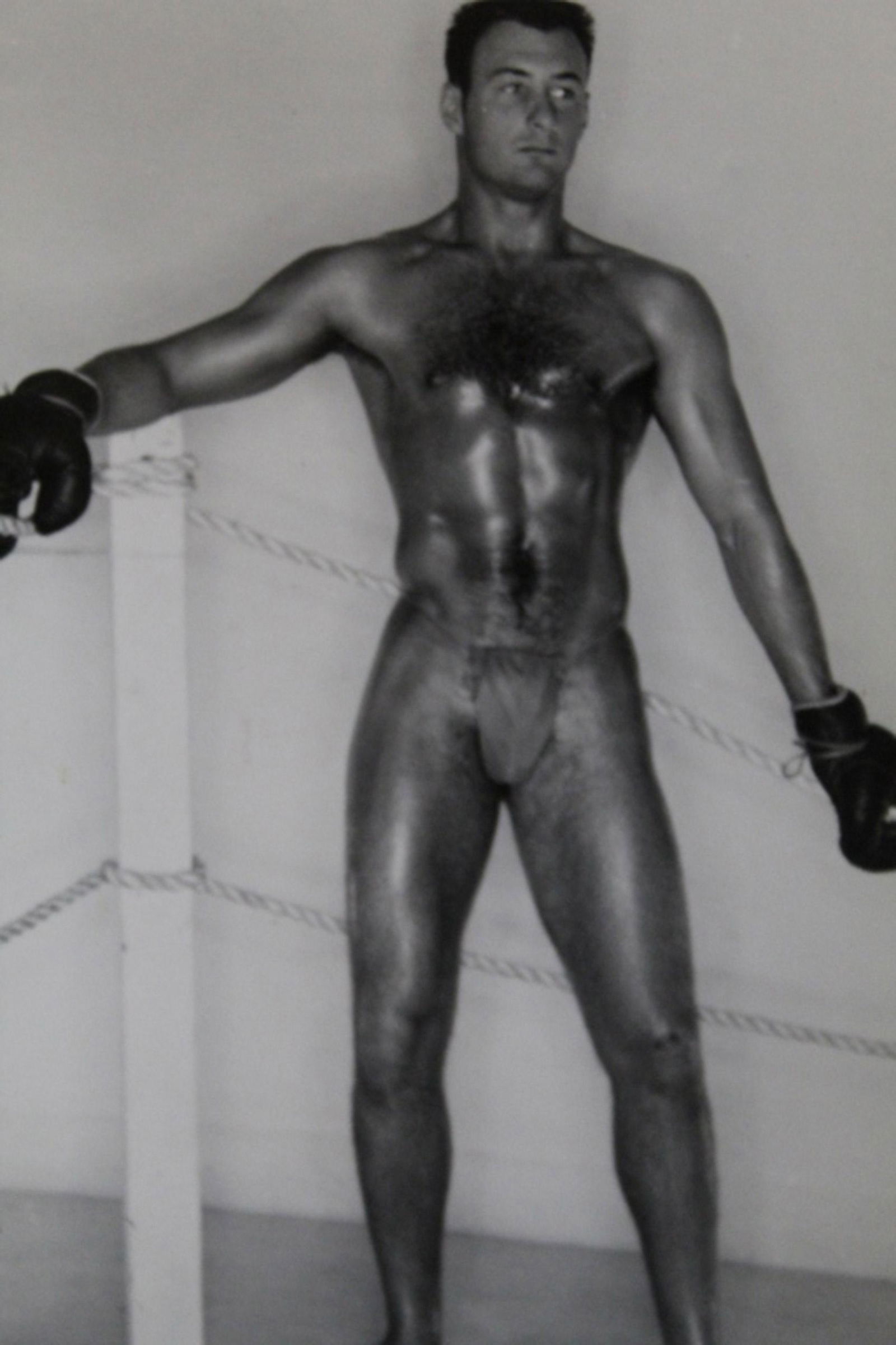 Bob Mizer AMG Male Semi Nude Photograph: Model in posing strap wearing boxing gloves. Pencil numbered 42 with number stamp to reverse. Good sharp image printed on semi-gloss paper. Circa 1950's. 4" x 5".