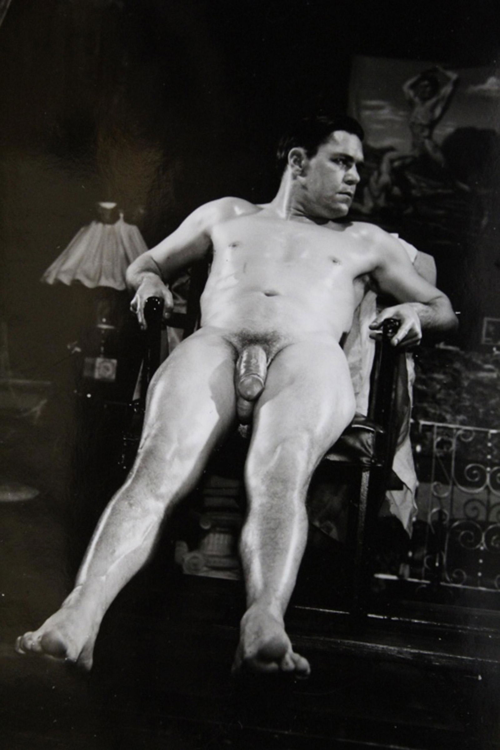 Bob Mizer AMG Male Nude Photograph: Nude model sitting on chair in stage set. Pencil notations to reverse. Good sharp image printed on gloss paper. Circa 1950's. 4" x 5".