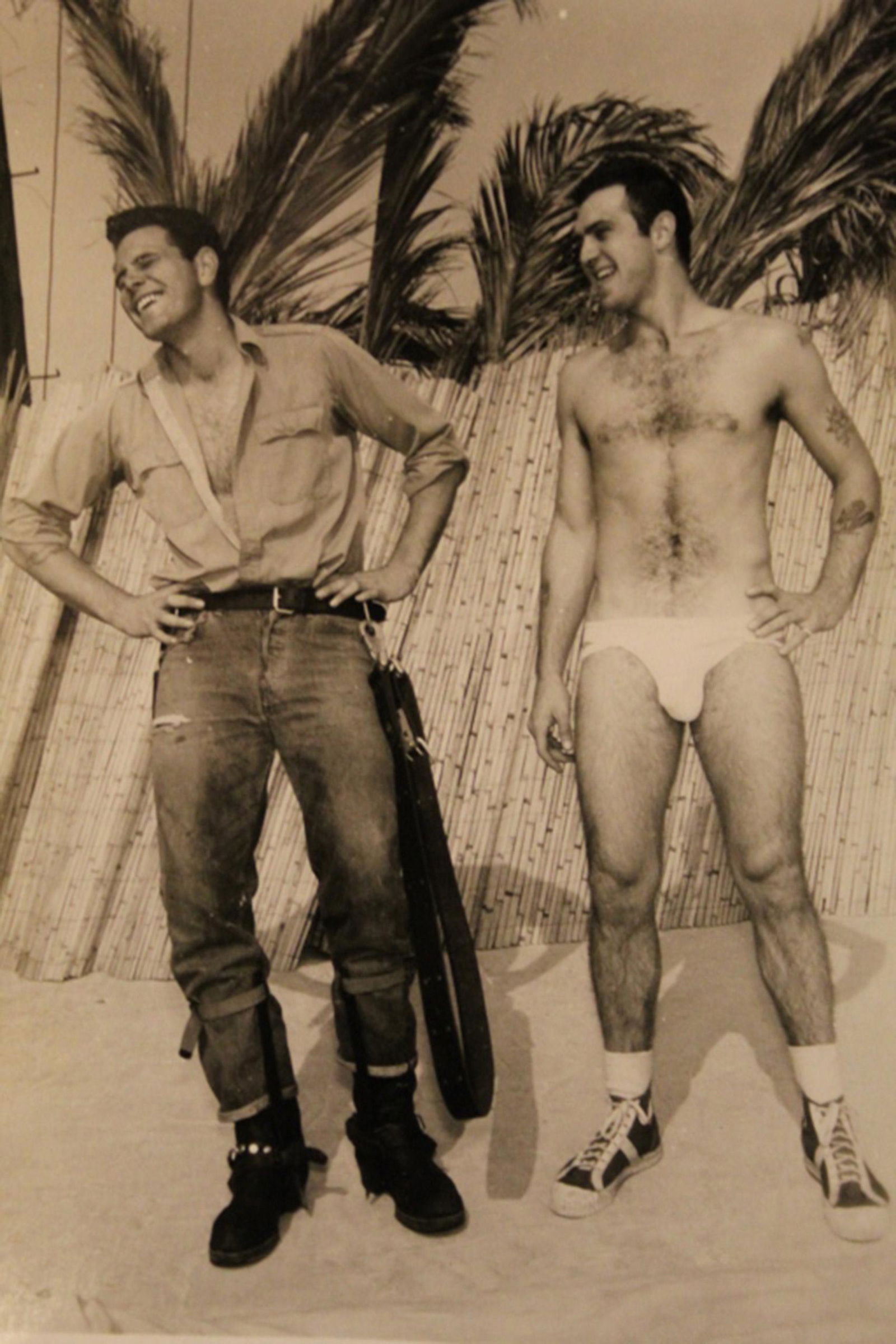Bob Mizer AMG Male Semi Nude Photograph: Image of two models; one model in jeans and motorcycle boots, the other tatooed model wearing a jockstrap and hightop basketball shoes. Pencil N D 39 notations to reverse. Good sharp image printed on