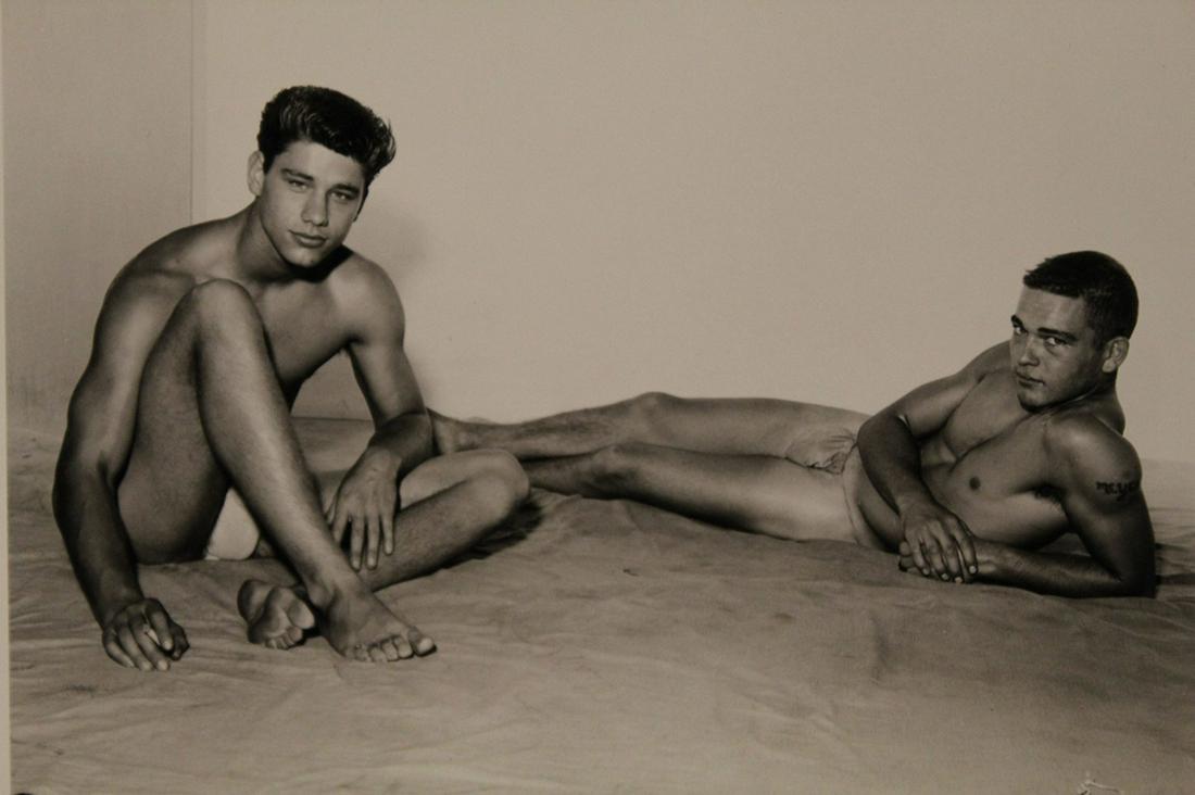 AMG Bob Mizer Male Semi Nude Photograph: Two models posed on canvas drop cloth with white background (one model with cigarette in hand). Pencil written 12 to reverse. Excellent clear sharp image on gloss paper. Circa 1950's. 4" x 5".