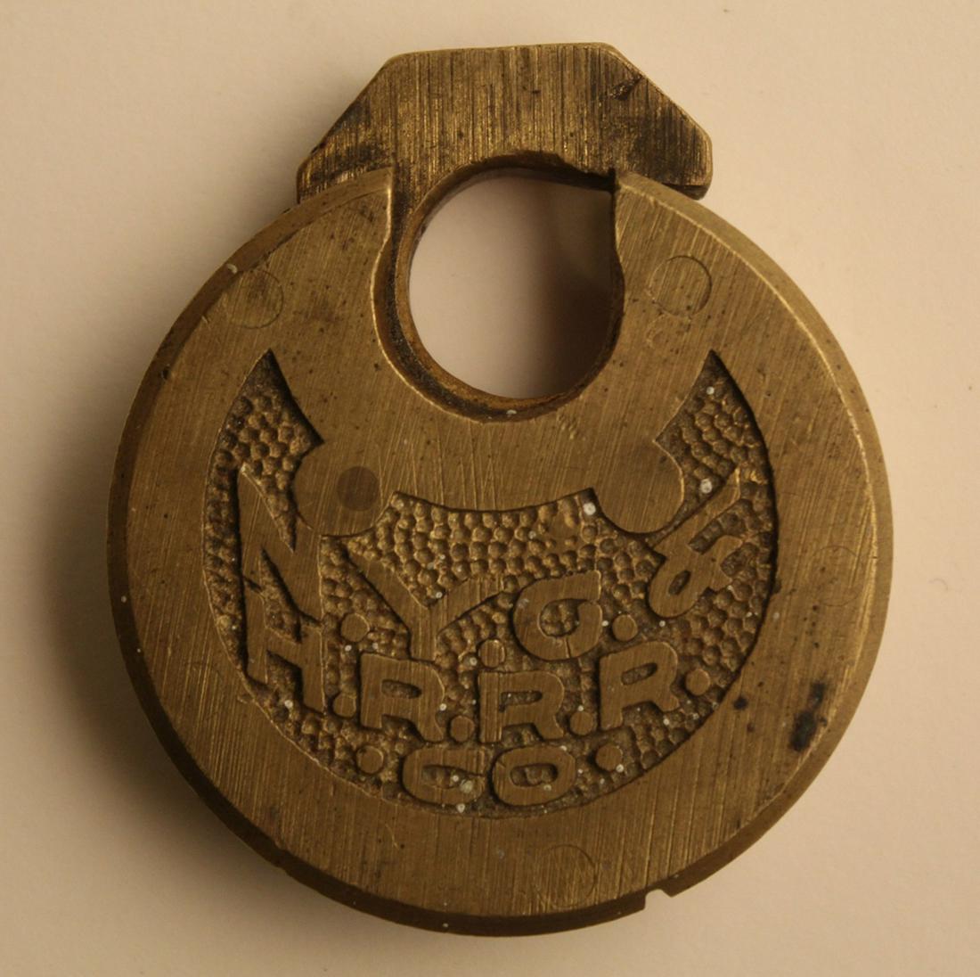 NYC & HRRR Railroad Pancake Padlock Lock: New York Central & Hudson River Rail Road cast brass pancake push padlock with raised lettering. Does not include key; movement to latch. Good old patina. 2.5" x 2.25" approx.