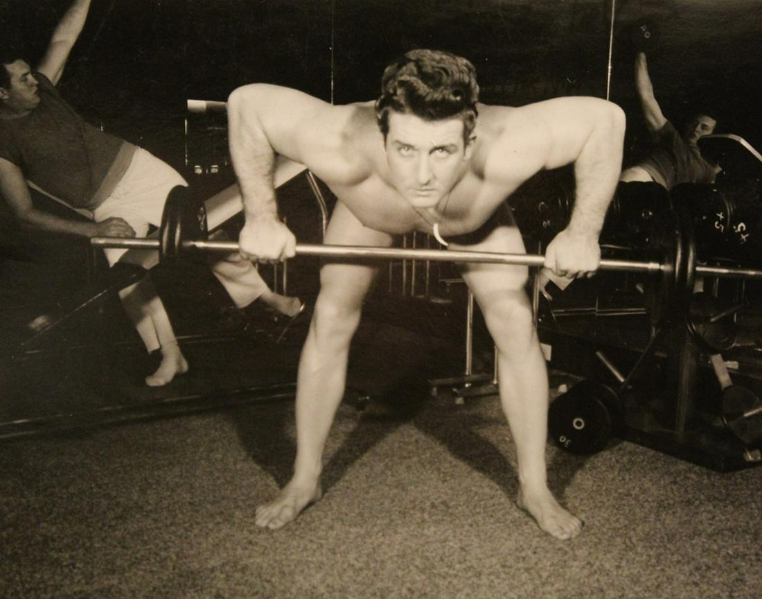 Vintage Bob Mizer AMG Semi Nude Male Photograph: Bodybuilder doing bent over barbell rows in a gym setting. Pencil written "5" to reverse. Excellent clear sharp image on semi gloss paper. Circa 1950's/ 60's. 4" x 5".