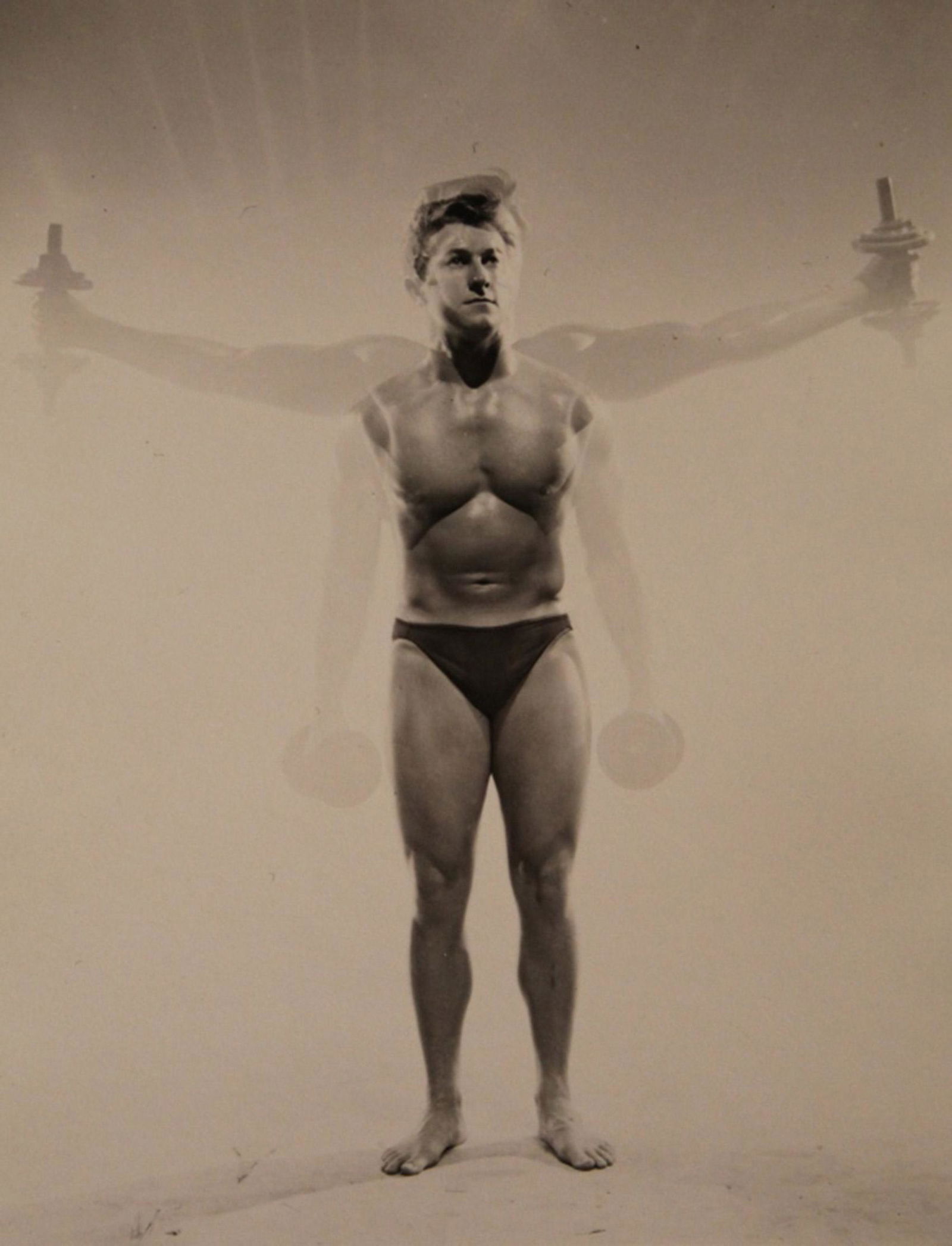 Vintage Bob Mizer AMG Semi Nude Male Photograph: Intentional double exposure image of a bodybuilder doing dumbell lateral raises. Partial number stamp to reverse. Excellent clear sharp image on semi gloss paper. Circa 1950's. 4" x 5".
