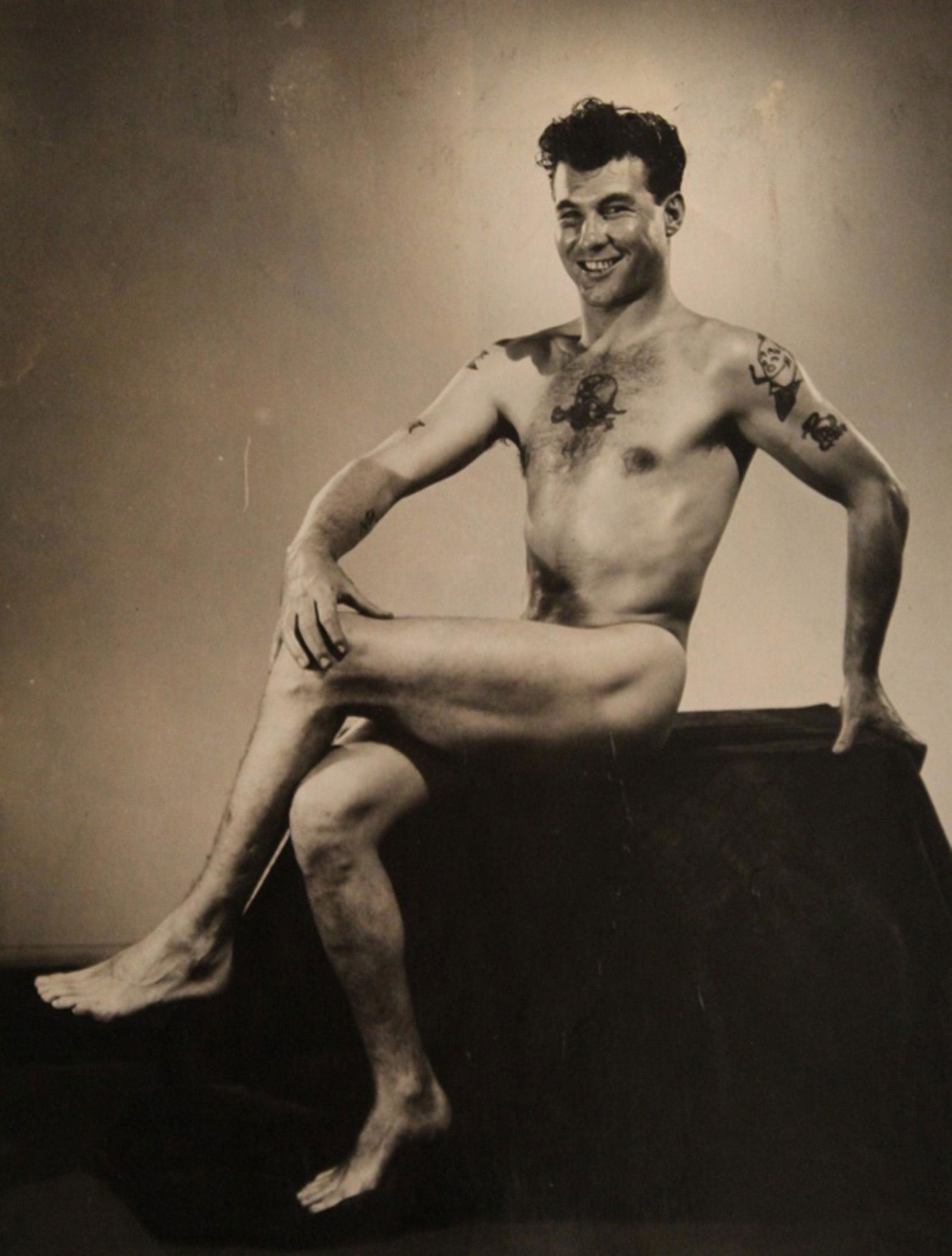 Vintage Bob Mizer AMG Nude Male Photograph: Nude model with tattoos posed on a fabric draped stand. Clear sharp image on semi gloss paper. Stamped "LI" to reverse.Good condition with some minor age wear, glue residue to the reverse (does not ef