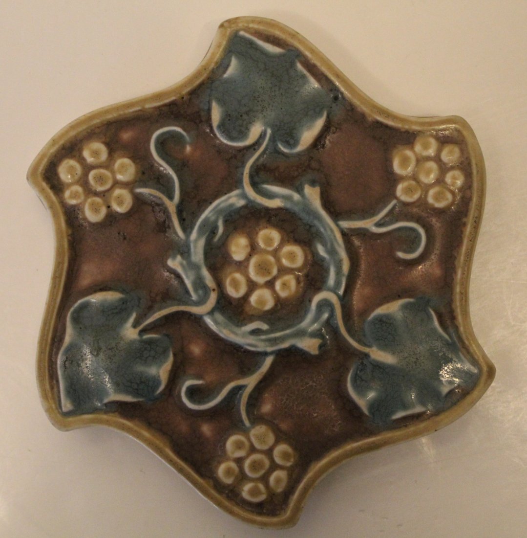 1919 Rookwood Pottery Trivet: Shape #3091 with raised grape and vine design. Impressed marks to underside. Very good condition; one hard to see small flea bite glaze "ding" to underside of one point. 6.25" dia.