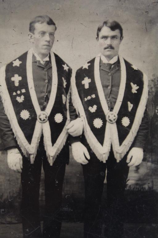 Tintype Photograph of Affectionate Men: Two men posed arm in arm wearing wide Masonic lodge collar sashes and gloves. Clear and sharp image with normal signs of age wear, etc. 3 1/2" x 2 3/8" approx.