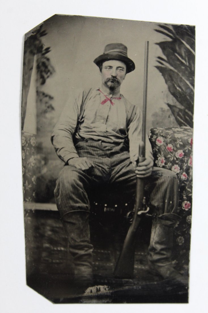 Antique Tintype Photograph Man with Rifle: Seated man posed with long rifle. Hand drawn and tinted string tie, tinting to his cheeks, and tinting to flowers of studio set fabric. Good clear sharp image with expected normal signs of aging, etc.
