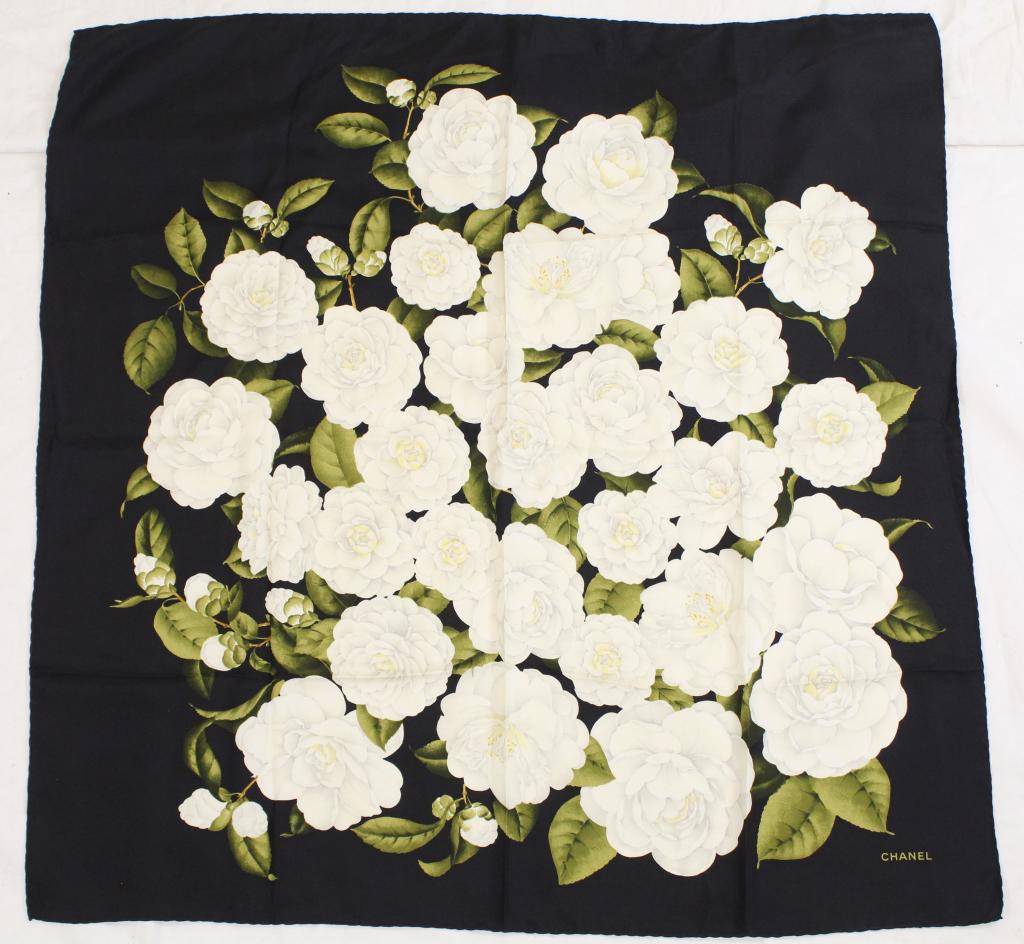Chanel White Camellia Flower Silk Scarf: White flowers and green leaves on black. Hand rolled and stitched edges. Very good condition with no apparent snags, pulls, spots, holes, etc. 34" x 34" approx.