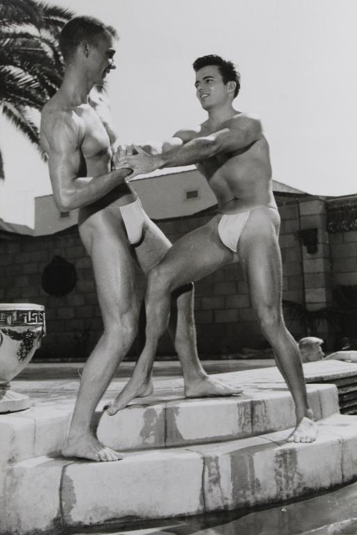 Bob Mizer AMG Male Nude Photograph: Two semi-nude male models photographed by the pool of Mizer's Los Angeles compound. Hand written "YPI-GE" in pencil to the reverse. Clear sharp silver gelatin print on satin heavy fiber paper. Circa 1
