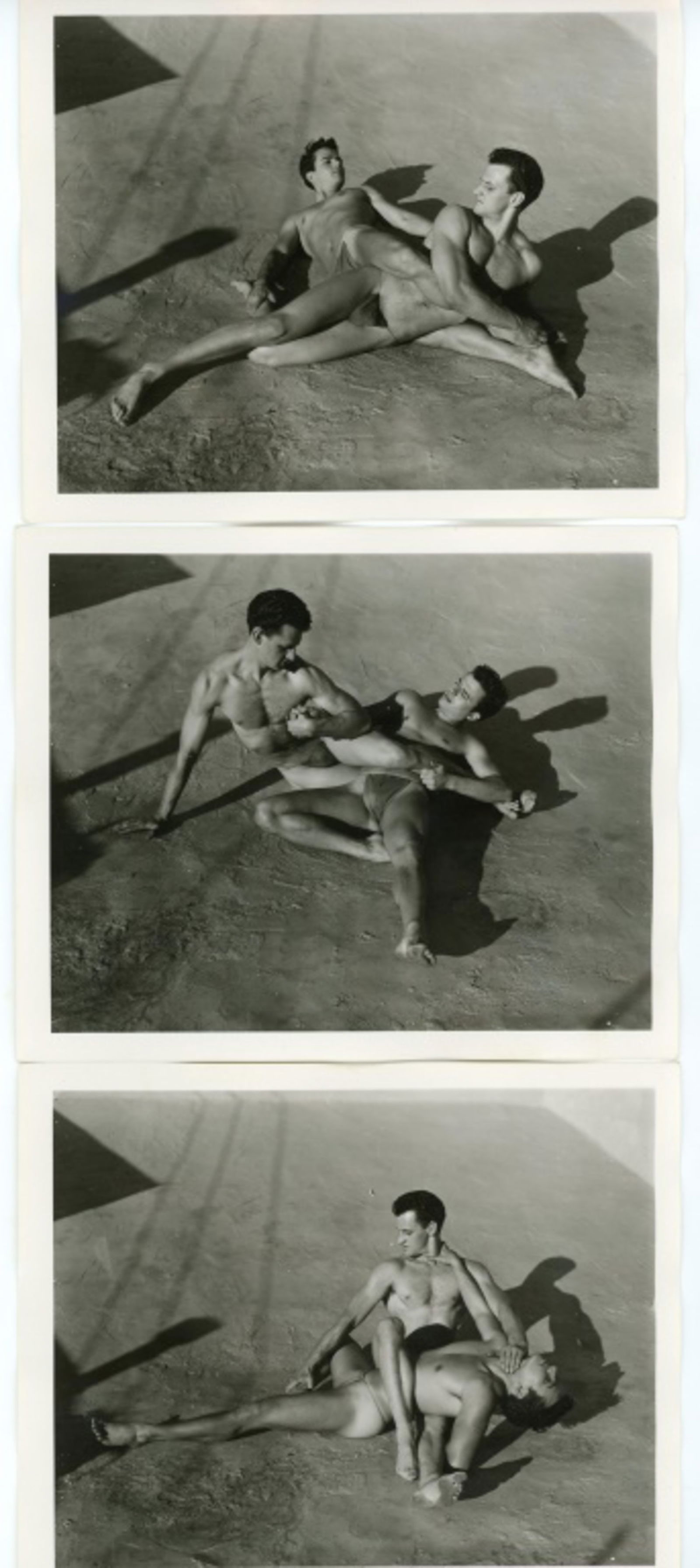 Vintage Bob Mizer AMG Male Physique Photographs: Three semigloss 4" x 5" photographs of two male models wearing posing straps wrestling on the AMG studio rooftop. Stamped 002R, 007R, and 008R to the backs; one dated FEB 56. Good condition. From the