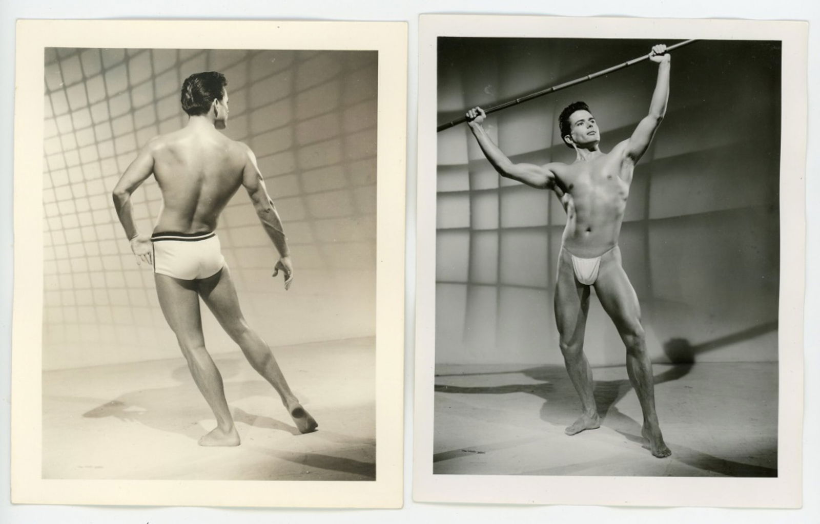 Vintage Bob Mizer AMG Male Physique Photographs: Two semigloss 4" x 5" photographs of male model posed in studio with projected netting background. (1) Posed with bamboo pole on semigloss paper. Pencil number 13 and partial stamp to the back. (2) Po