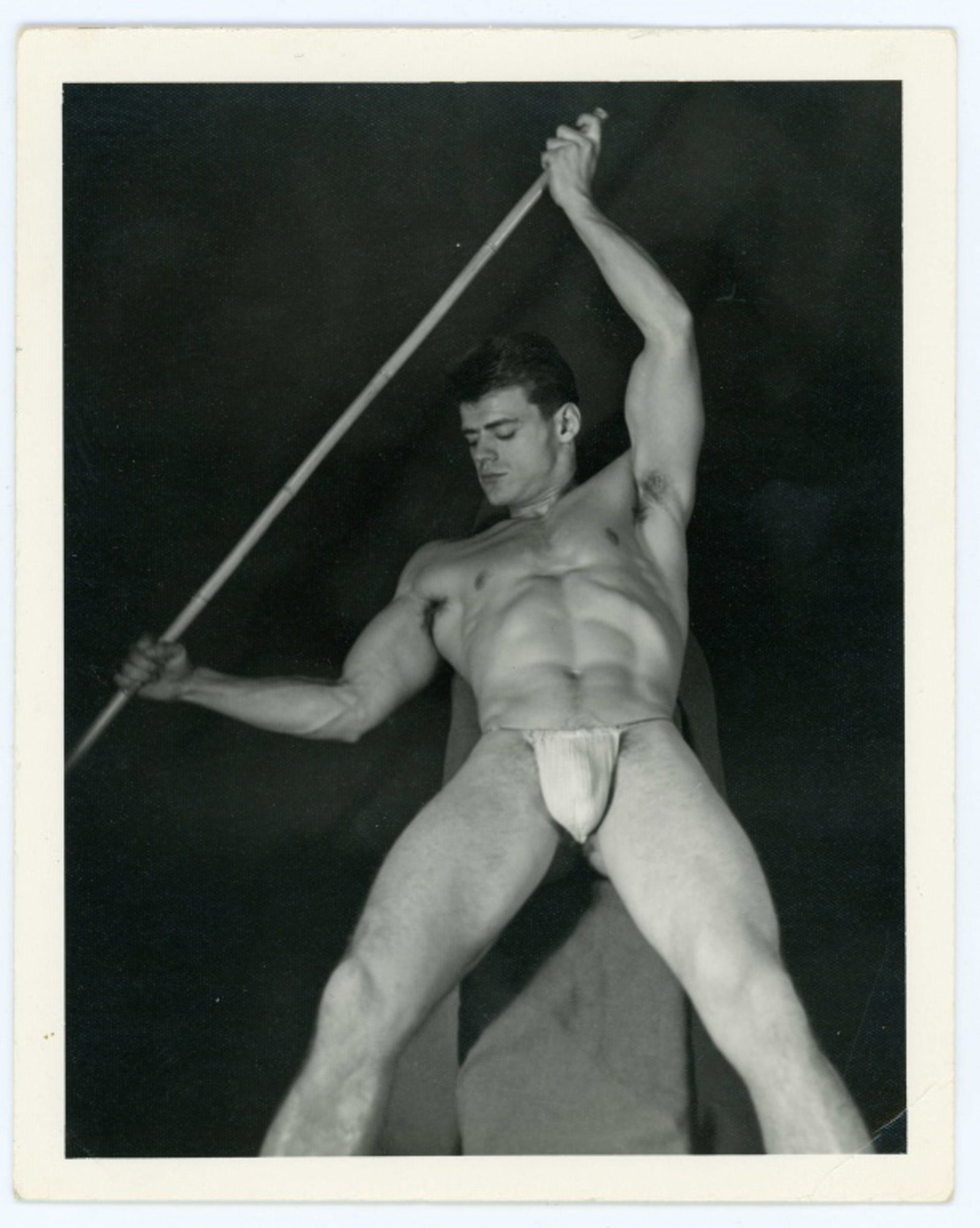 Kris Studio Male Physique Photograph: Vintage original 4" x 5" Chuck Renslow / Kris Studio photograph of model in posing strap holding a bamboo pole. Not numbered or stamped. Clear sharp image on double weight textured paper; crease to lo