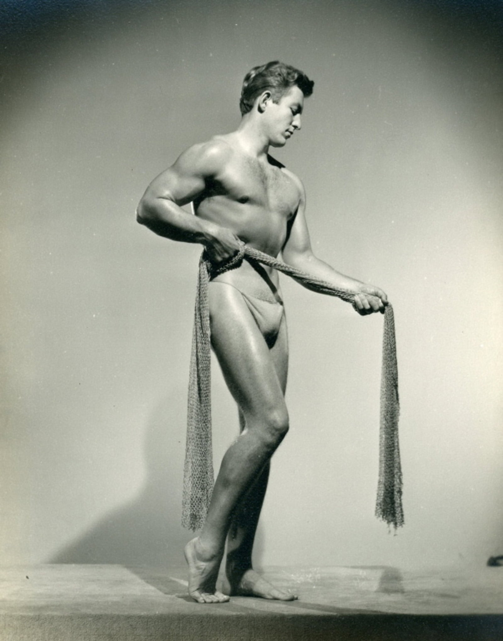 Spartan of Hollywood Male Physique Photograph: Vintage original 5" x 4" photograph by Spartan of Hollywood (Constantine Hassalevris) of model Ed Kysar posed with netting. Unstamped. Clear sharp image without borders on slightly textured double wei