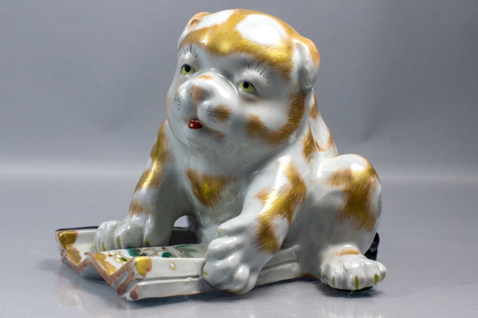 Antique Japanese Kutani Porcelain Dog Puppy: Early 20th century hand decorated Japanese Kutani porcelain puppy sitting on a folding fan. Unmarked. Good condition. 4 3/4" H x 5 5/8" x 4 1/4" approx.