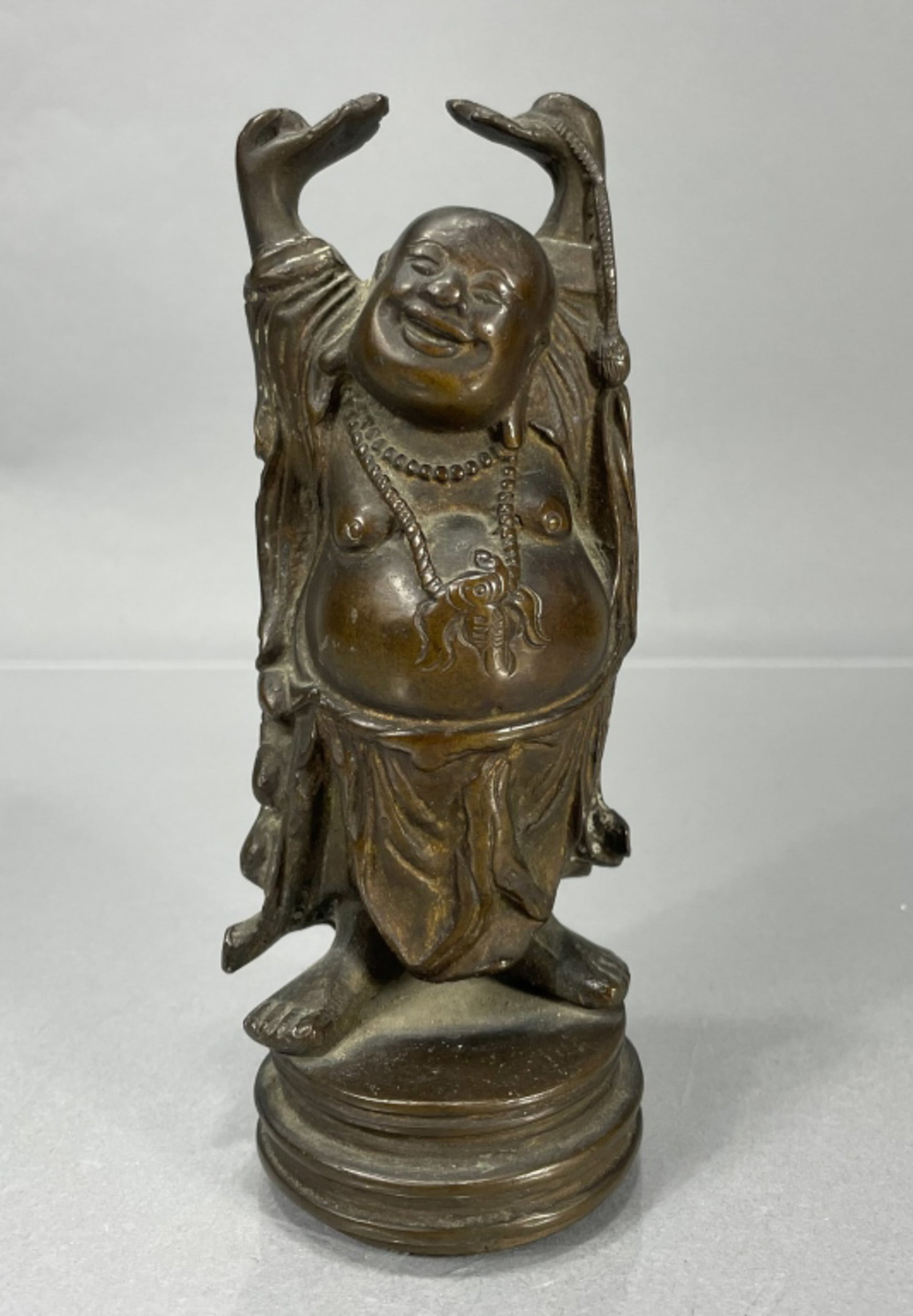 Chinese Bronze Standing Hotei figure Arms Raised: Chinese bronze standing smiling Hotei figure with arms raised. Wearing ritual necklace, peach branch hanging on back of robe. Light surface wear. 6.5" high.