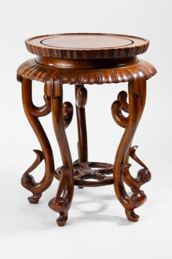 Chinese Carved Hardwood Pieced Wood Stand: Chinese hardwood vase stand with a pale yellow-brown finish. Gouged lappet designs around top, supported by five legs each with scroll and leaf design. Openwork wheel roundel attached to bottom. All t