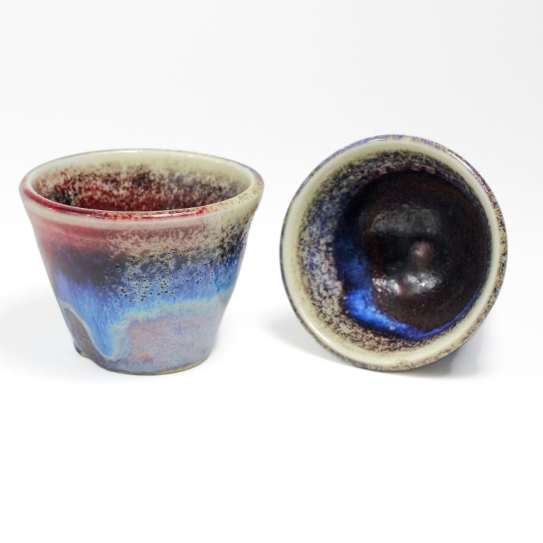 Pair Chinese Porcelain Flambe Glaze Tea Cups: Pair of Chinese porcelain tea cups, with highly varigated flambe glaze throughout. One cup with glaze flaking and chip to footrim. Unmarked. Each 1.75" H x 2.25" diameter approx.