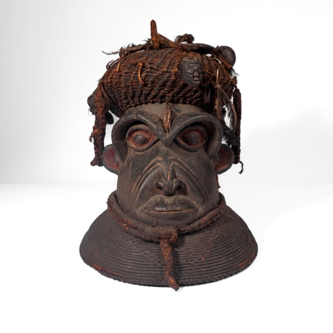 Tall African Wood & Cane Headdress: Tall African Wood & Cane Headdress. Base comprised of tightly woven cane with carved wood face sitting above, adorned with various cords, feathers, hollow seeds and carved effigies. In good condition,