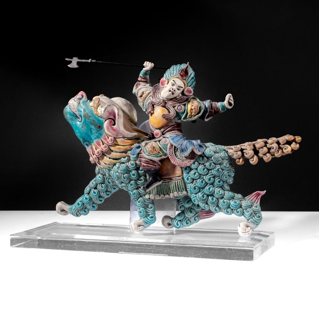 Chinese Ceramic Warrior Riding Lion Roof Tile: Chinese polychrome-glazed ceramic roof tile depicting a warrior riding shishi / foo lion with painted polychrome glazes and incised details to garments and steed. Includes removable metal halberd. Pro