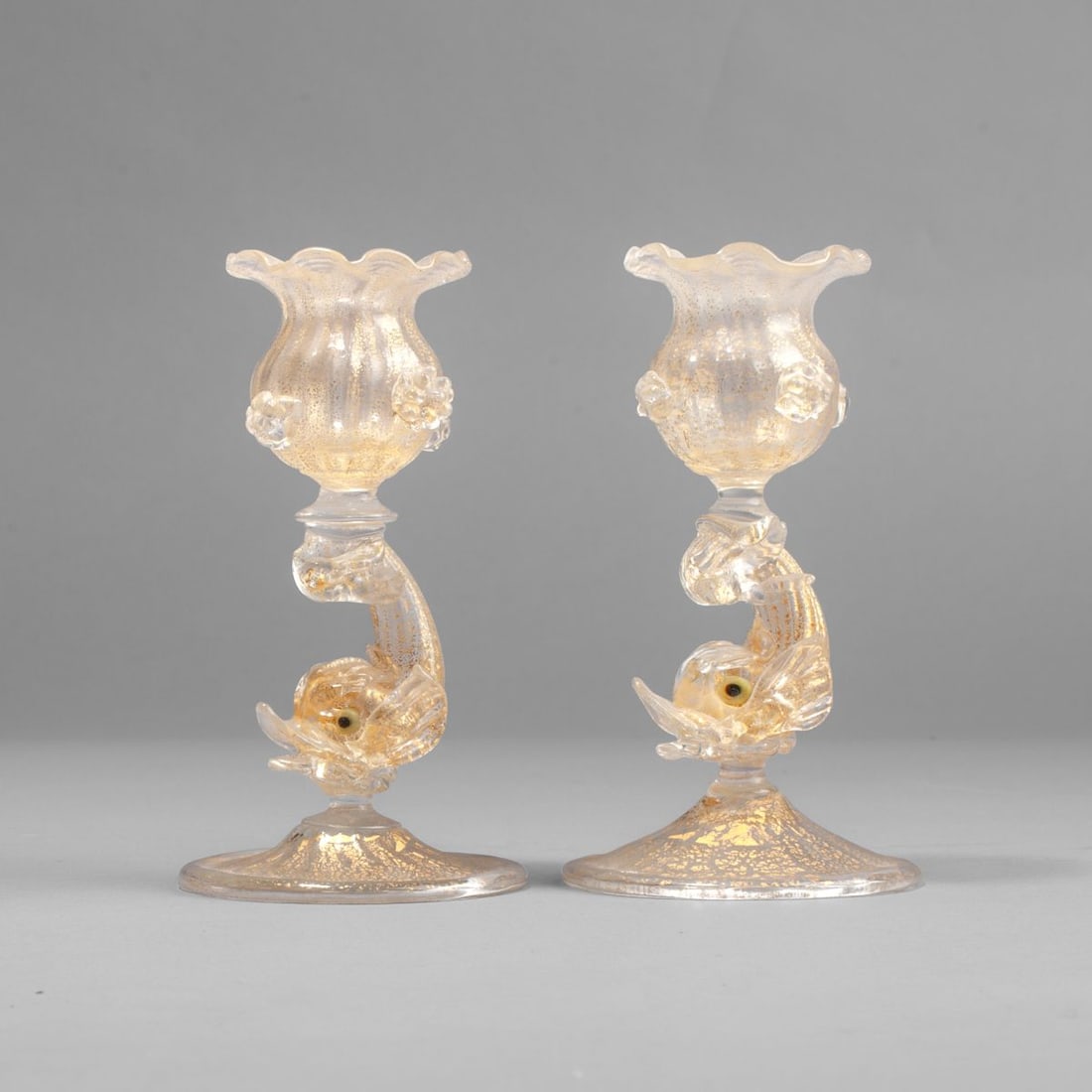 Murano Glass Gold Flecked Dolphin Candlesticks: Pair of Murano glass candlesticks, the clear gold-flecked glass showing dolphins above ribbed circular bases below scalloped cups with applied fruits. Both in very good condition. 4.75" H ea.