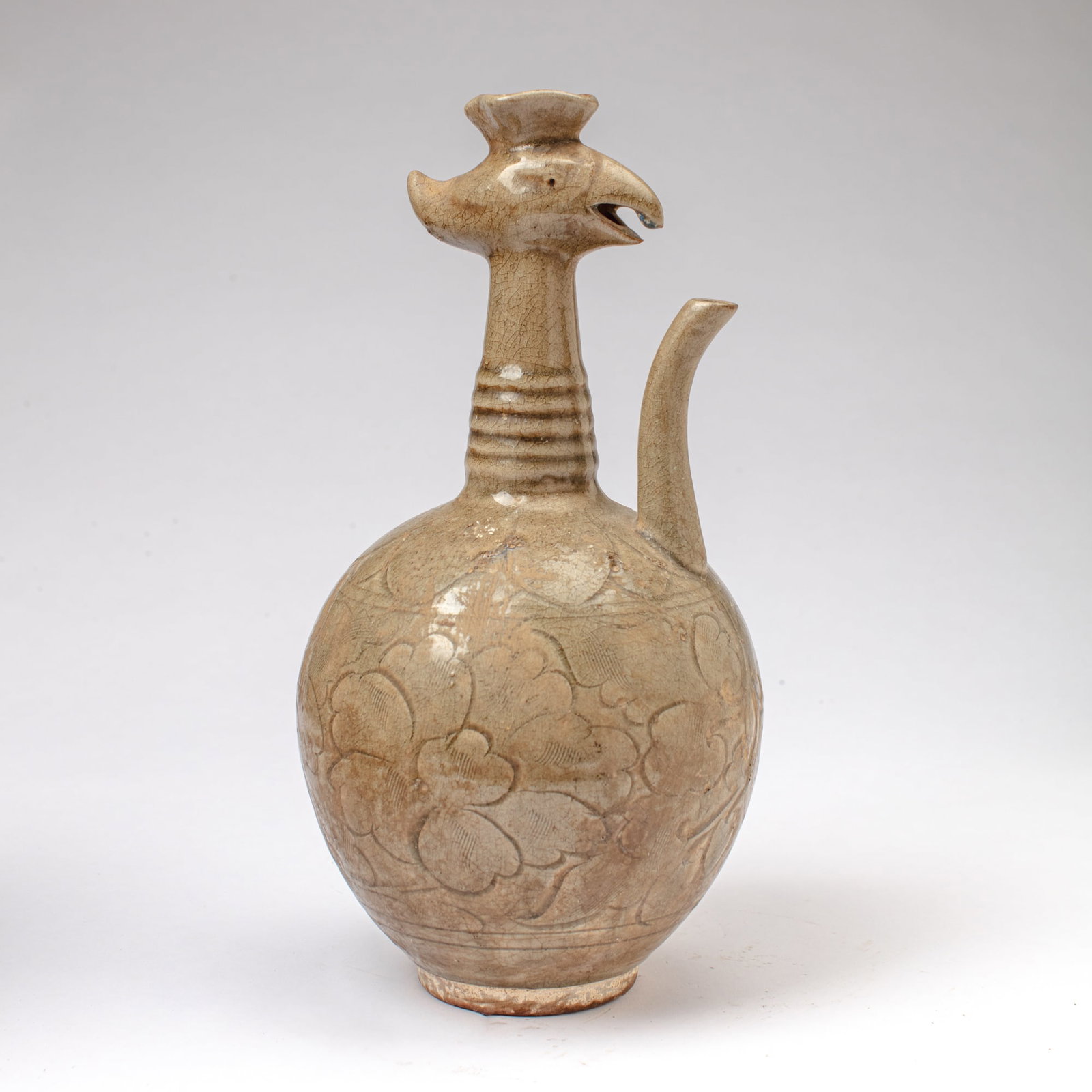 Chinese Celadon Glaze Phoenix-Head Ewer: Chinese celadon-glazed ewer of boulbous form with ribbed neck rising to opening having phoenix head modeled in relief, the body with incised peony flowers below band of leaves. Surface wear; kiln grit