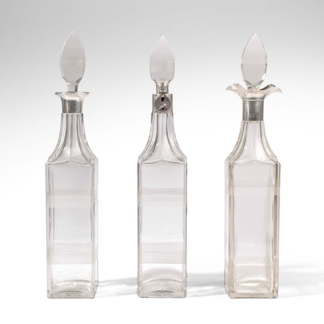 Sterling & Glass Decanters w/ Lock & Key 1923: Group 3 English sterling and glass spirit decanters with cut reed band sides and star bottoms. (1) Decanter fitted with sterling mechanism to lock stopper in place; includes working key. Hallmarks for