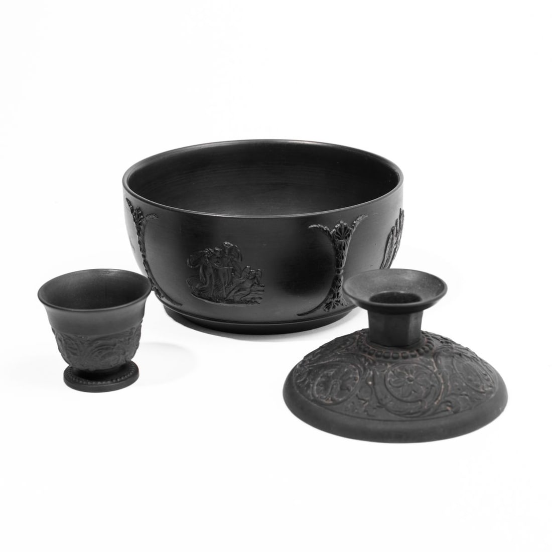 Wedgwood Black Basalt Candlestick / Cup / Bowl: Three early 20th century Wedgwood black basalt pieces. (1): Candlestick with raised anthemion pattern. Impressed "WEDGWOOD" and "ETRURIA ENGLAND" marks to underside. In very good condition 2" H x 3.75