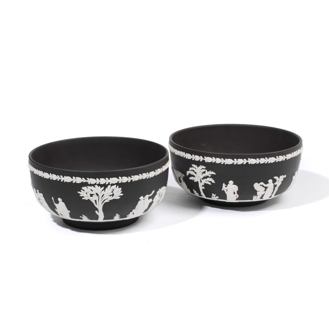 Pair Wedgwood White Dip & Black Basalt Bowls: Pair of 20th century Wedgwood black basalt bowls with scenes of classical figures below oak leaves and acorns in white. Impressed "WEDGWOOD" and "MADE IN ENGLAND" marks to underside. Some slight