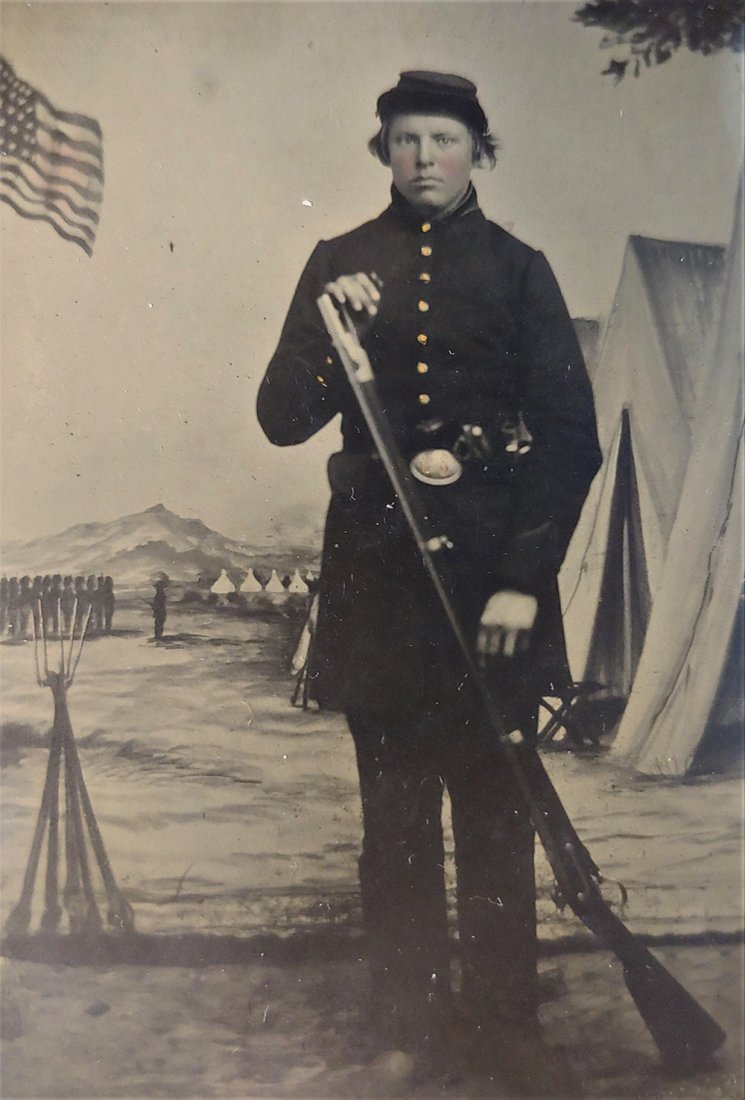 1/4 Pl. Tintype Civil War Soldier at Camp Michigan: Early war Union Soldier is posed in front of the known and recognizable backdrop of Camp Michigan. Likely 1862. He displays a large bore model 1842 musket, and has a Colt revolver tucked in his belt. 