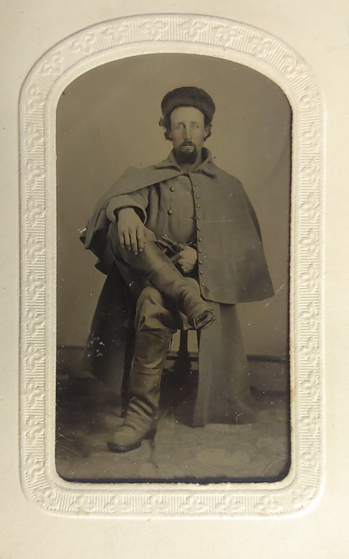 Civil War Tintype Trooper in Greatcoat & Boots (8th PVC?): Near mint CDV size tintype in paper mount of a dashing cavalry trooper wearing his caped overcoat, and a pair of magnificent cavalry boots. He clasps a pair of fine quality dark leather riding gloves 