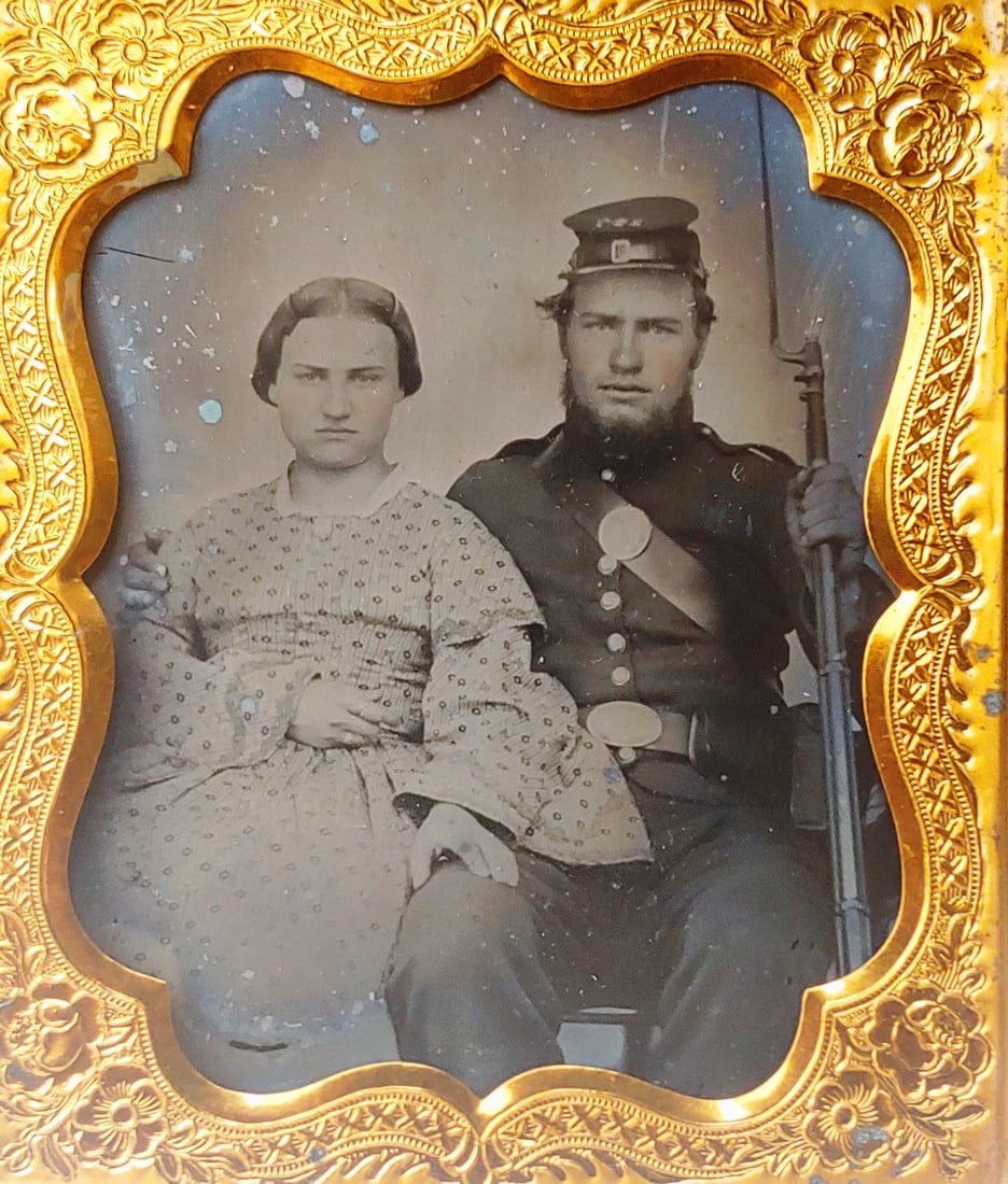 Cased Sixth Plate Ambrotype Armed Civil War Soldier & Wife: Very fine early Civil War image in top shelf condition. Uniformed soldier displays his musket and accoutrements, while his wife sits stoically by his side. Housed in a full case. $22 for packing, UPS