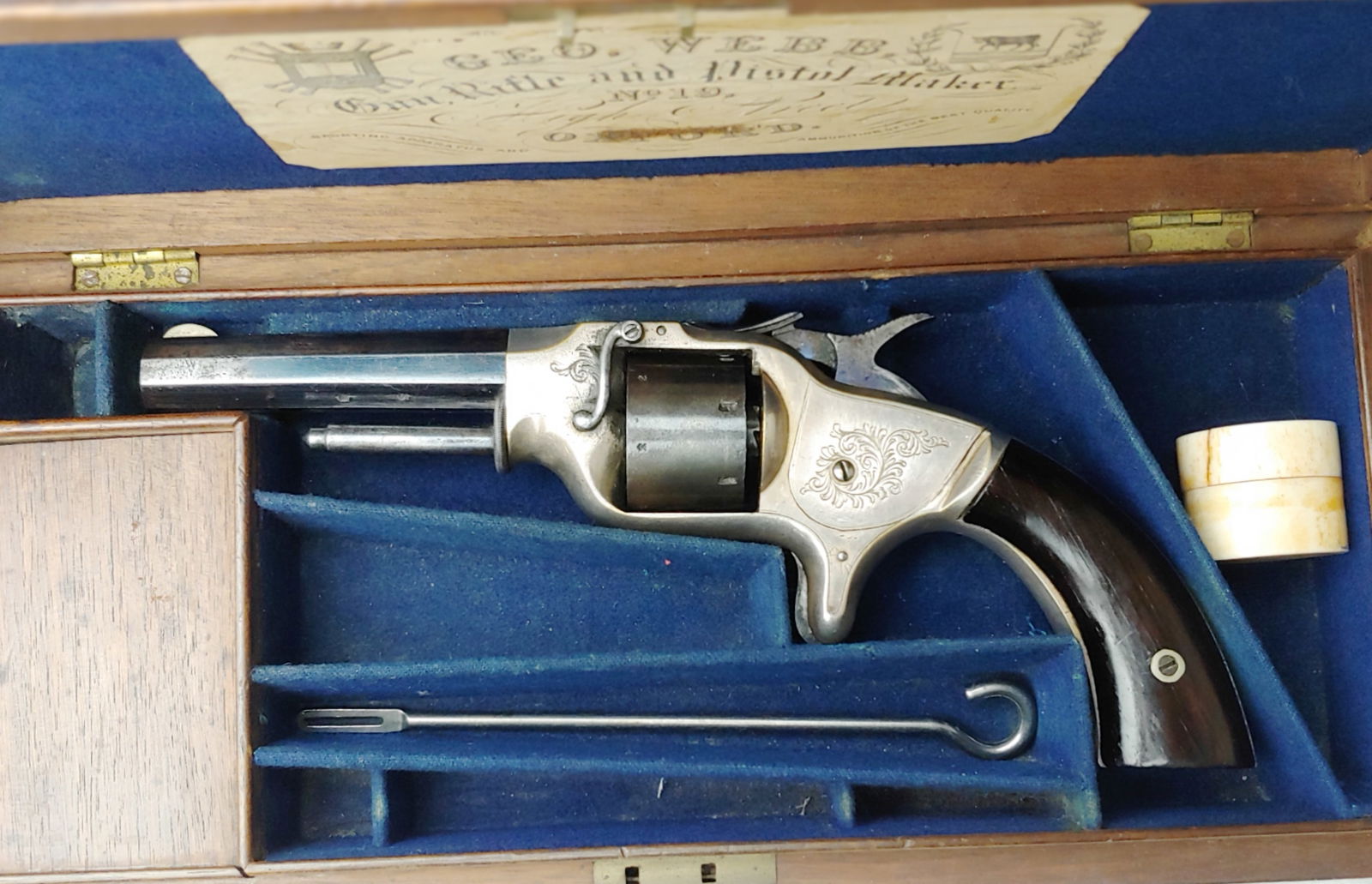 Fine Webb Revolver in Original Casing with Soldier's Name & Crest on Lid: Extremely rare George Webb, Oxford, England, cased and engraved 7 shot cartridge revolver with a 4 inch barrel in fine condition. The Caliber is 32 rimfire, same as Smith and Wesson. The box of 32 rif