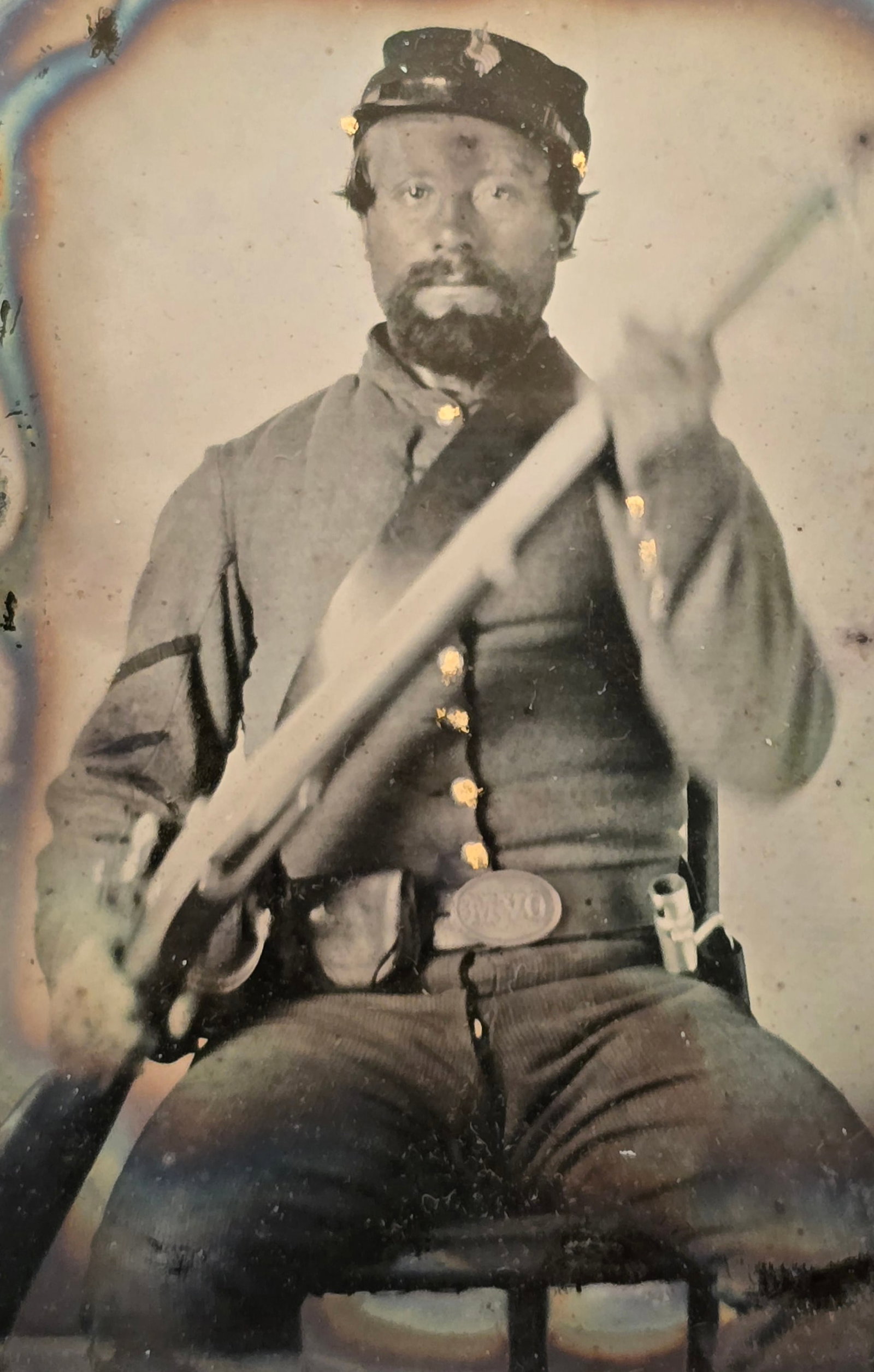 OVM Buckle Ambrotype?: This sixth-plate Civil War ambrotype depicts a seated Union corporal from the Ohio Volunteer Militia (OVM) posing with his percussion rifle-musket held diagonally across his torso. He wears a classic 