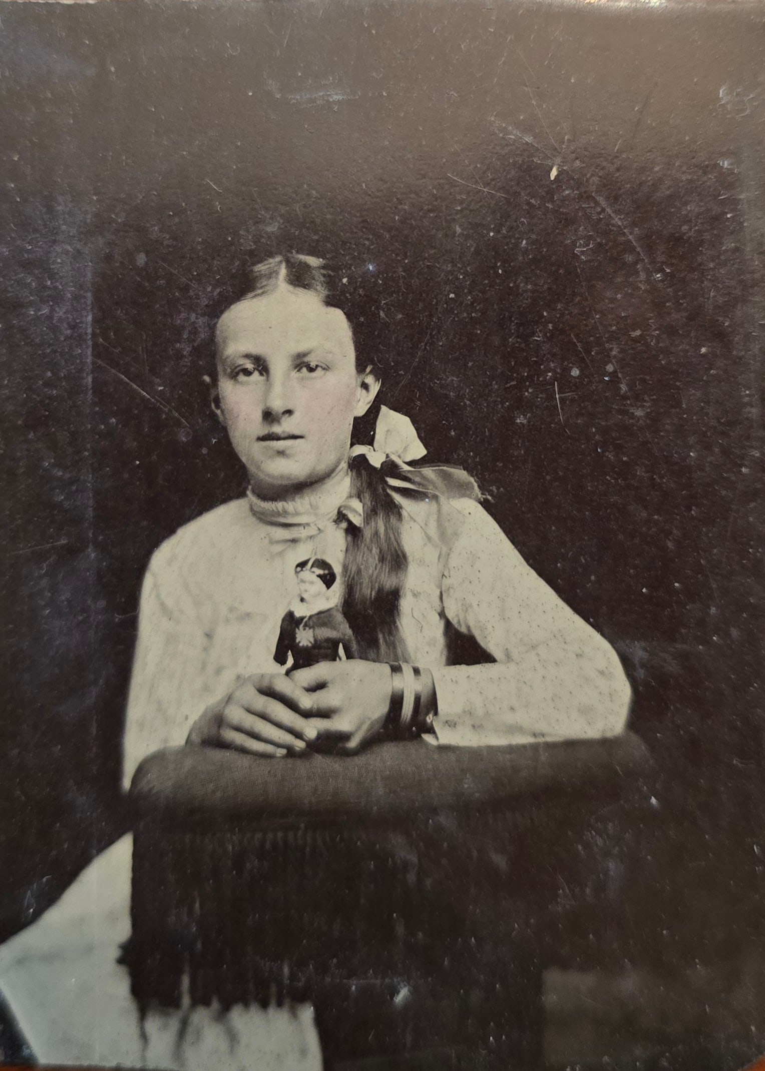 Wonderful 1860's Tintype of Girl and her Doll. Papa's Pride & Joy: This 1/6th plate cased tintype features a half-length seated depiction of a young girl holding a small, fully dressed doll prominently in her clasped hands. She wears a high-collared, light-colored bl