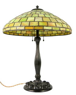 A Tiffany style leaded glass table lamp, the marbled: A Tiffany style leaded glass table lamp, the marbled green pane shade on a baluster lobed patinated bronze base, 20th century, 48cm diameter, 61cm high