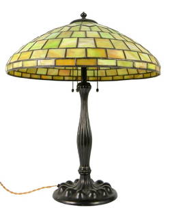 A Tiffany style leaded glass table lamp, the marbled: A Tiffany style leaded glass table lamp, the marbled green pane shade on a baluster lobed patinated bronze base, 20th century, 48cm diameter, 61cm high