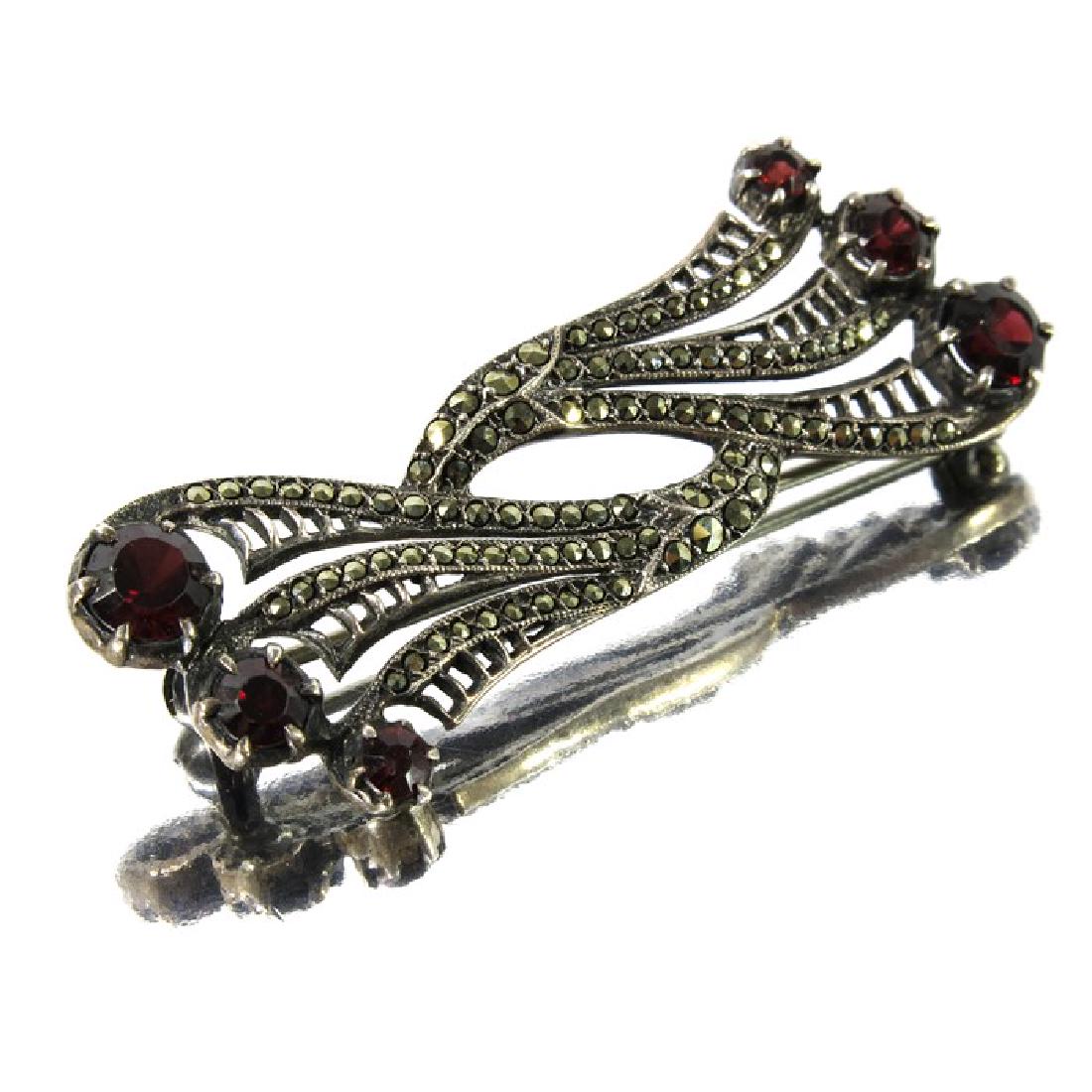 Bernard Instone, an Art Deco silver, marcasite and: Bernard Instone, an Art Deco silver, marcasite and garnet brooch, circa 1925, stylised pierced interlocking trumpet flowers with graduated terminals, stamped marks, 5cm