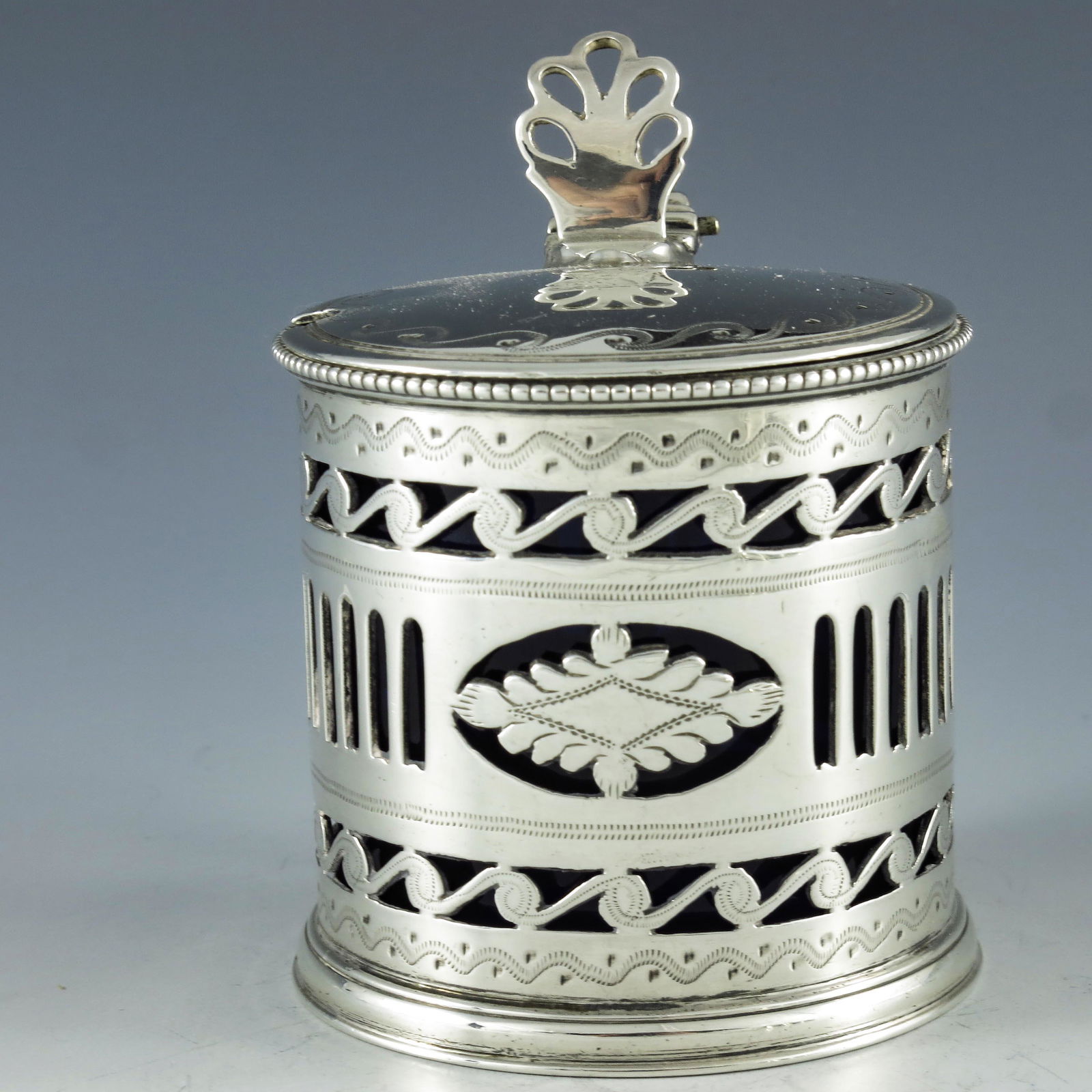 Charles Stuart Harris, London 1924, a George V silver: Charles Stuart Harris, London 1924, a George V silver mustard pot, cylindrical form reticulated and bright cut with Vitruvian scrolls, foliate lozenges and galleried banding, ear handle and beaded rim